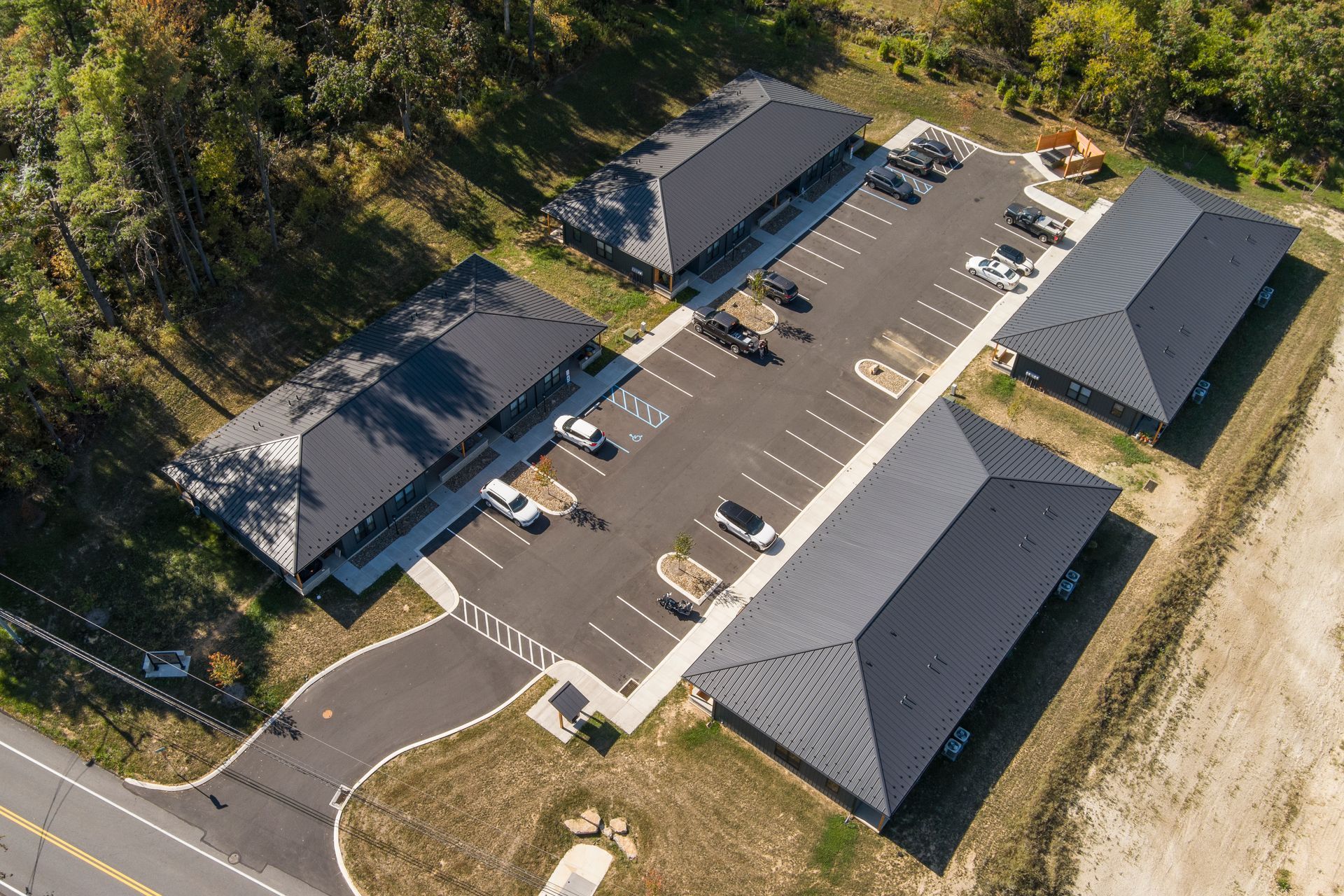 Aerial view of a complex with three dark metal roofed buildings, a parking lot, and access road