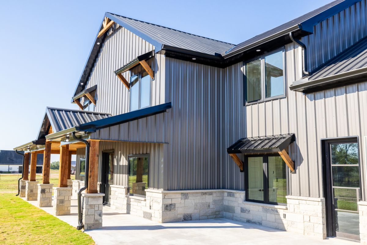 Gray metal-sided building with dark roof and trim. Stone and wood accents, sunny outdoor setting.