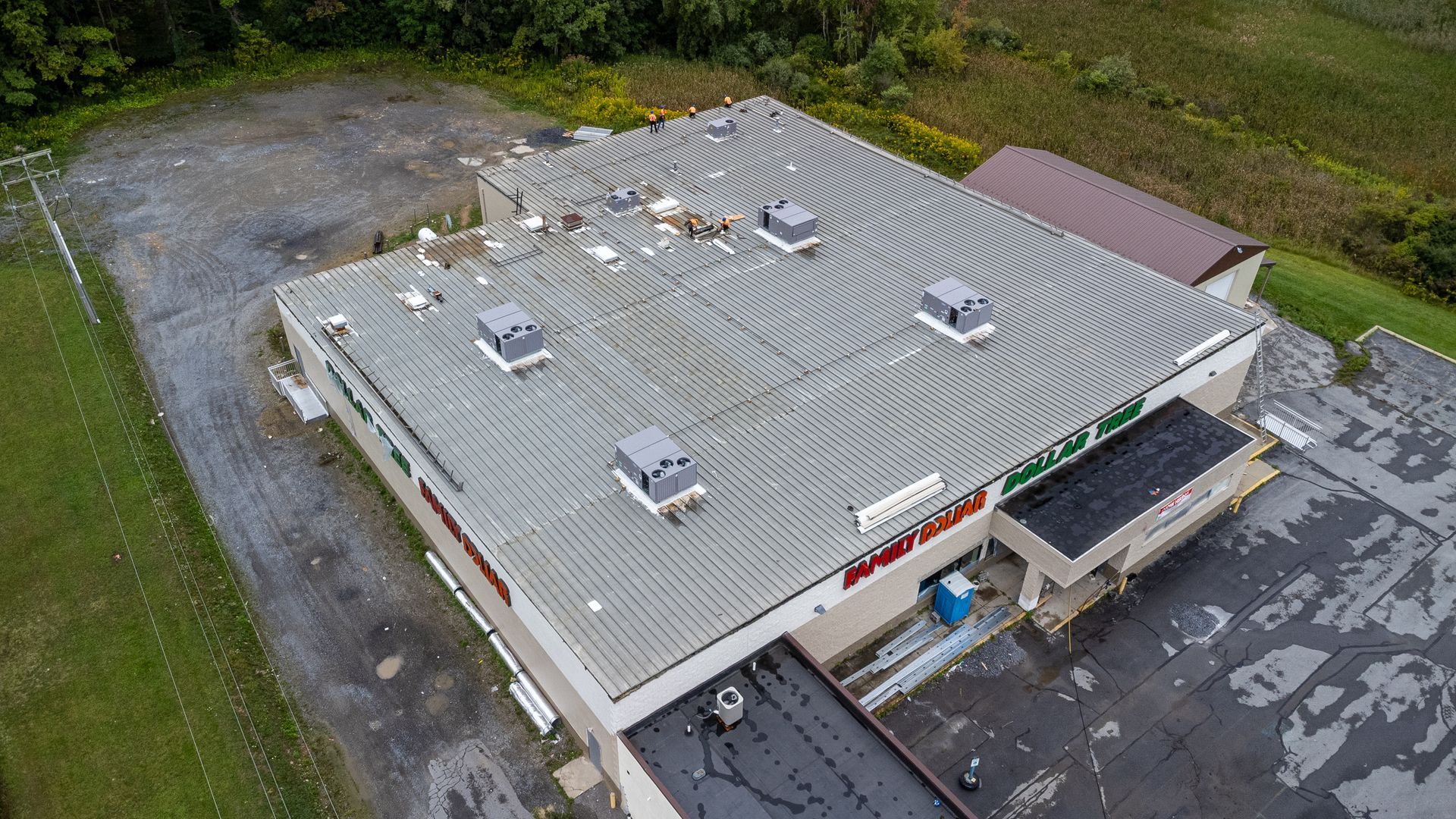 Aerial view of a commercial building with a damaged roof, surrounded by a parking lot and greenery.