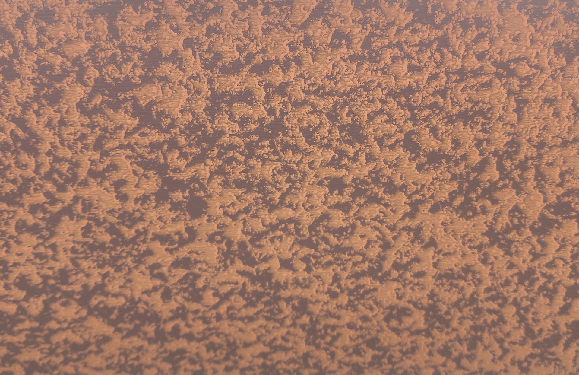 Rough, textured, orange surface, with varying highlights and shadows, likely a wall or painted object.