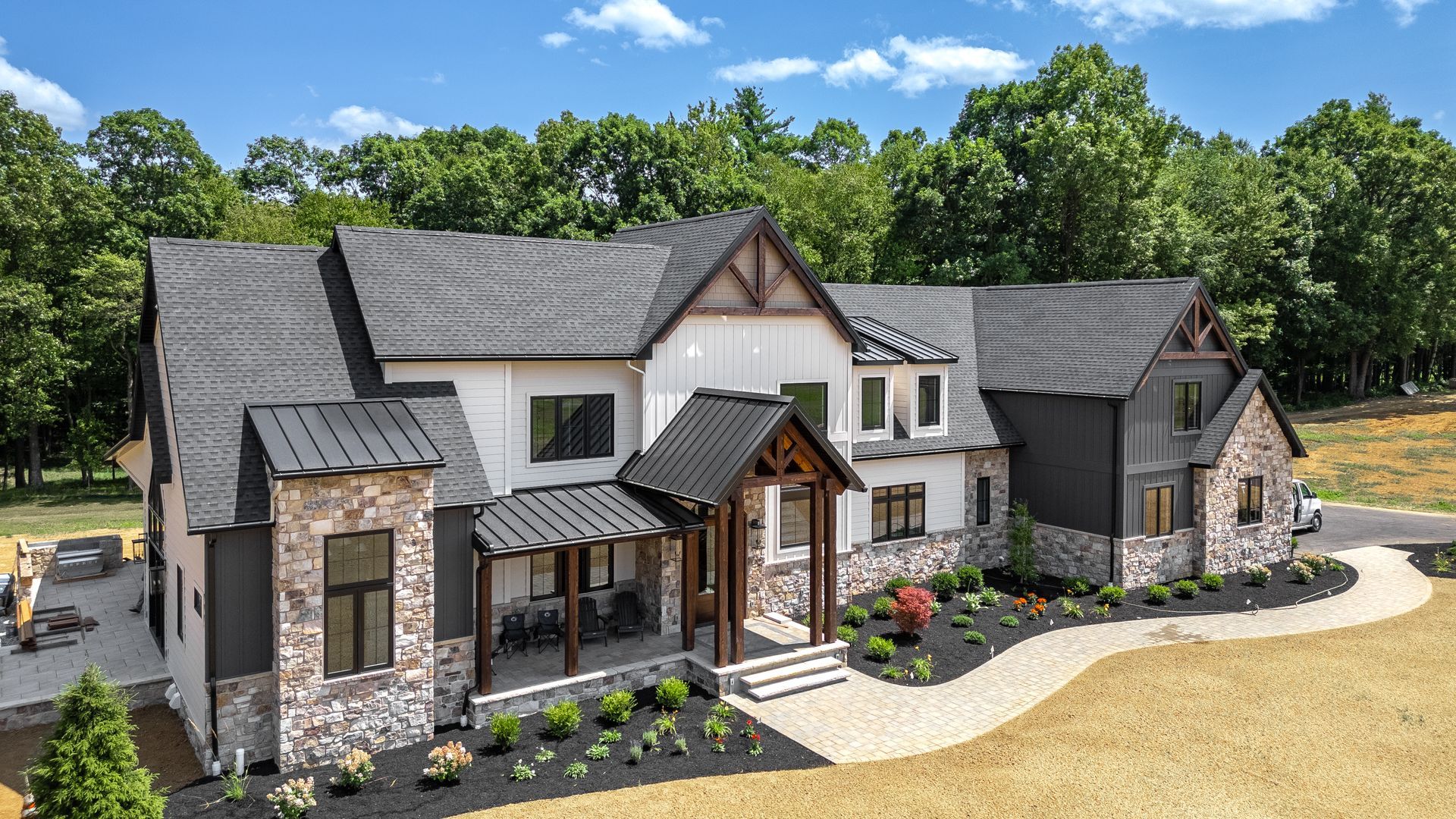Large modern farmhouse with black roof, white siding, stone accents, and landscaped front yard.