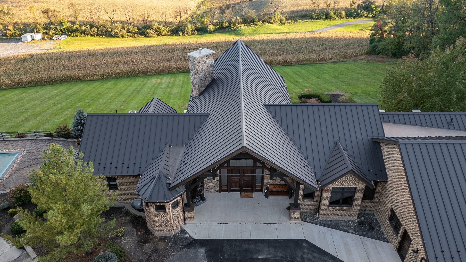 Aerial view of a modern, stone house with a dark gray roof, surrounded by green fields.