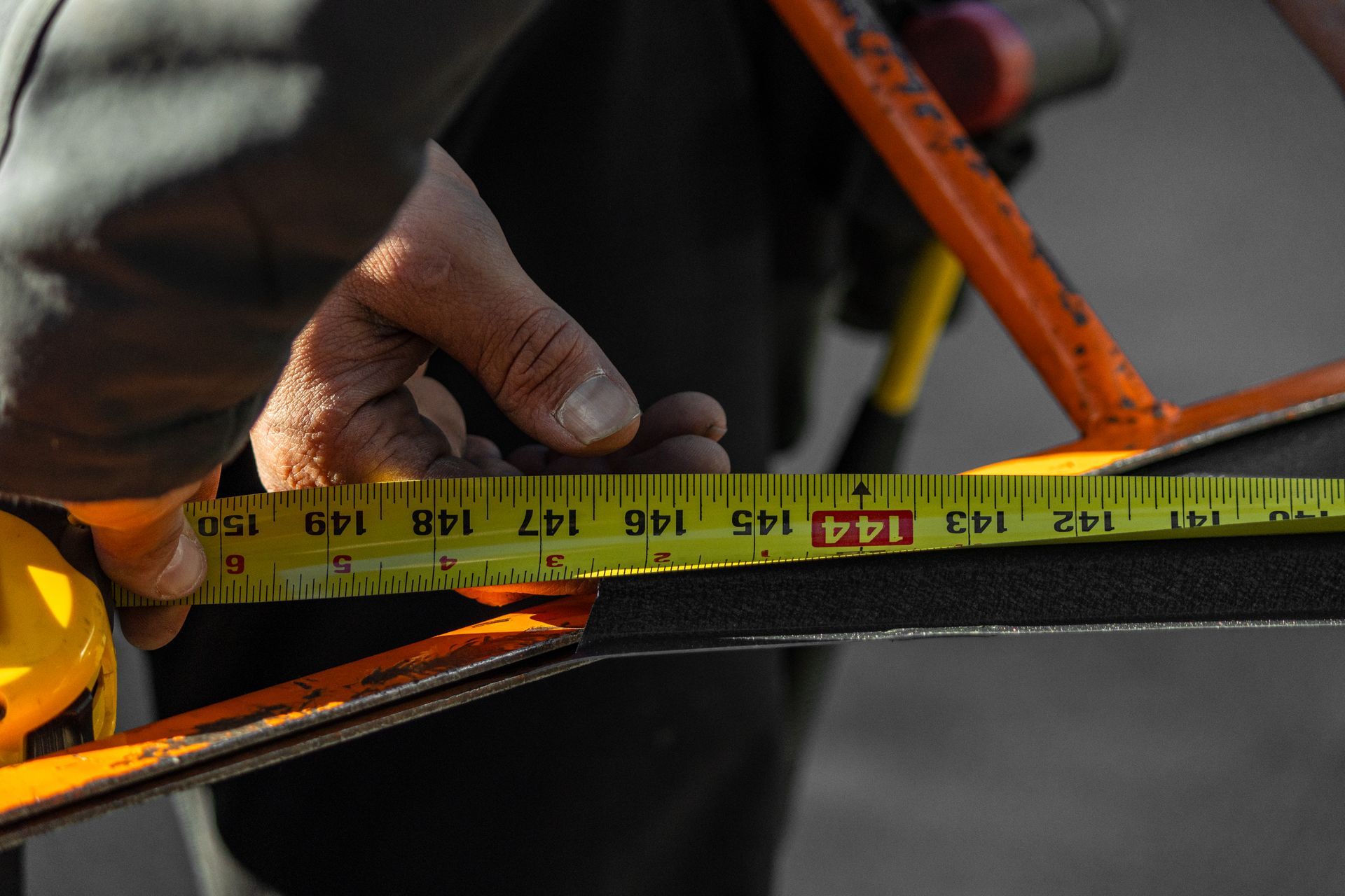 Person measuring with a tape measure, marking a black surface with the number 144 visible.