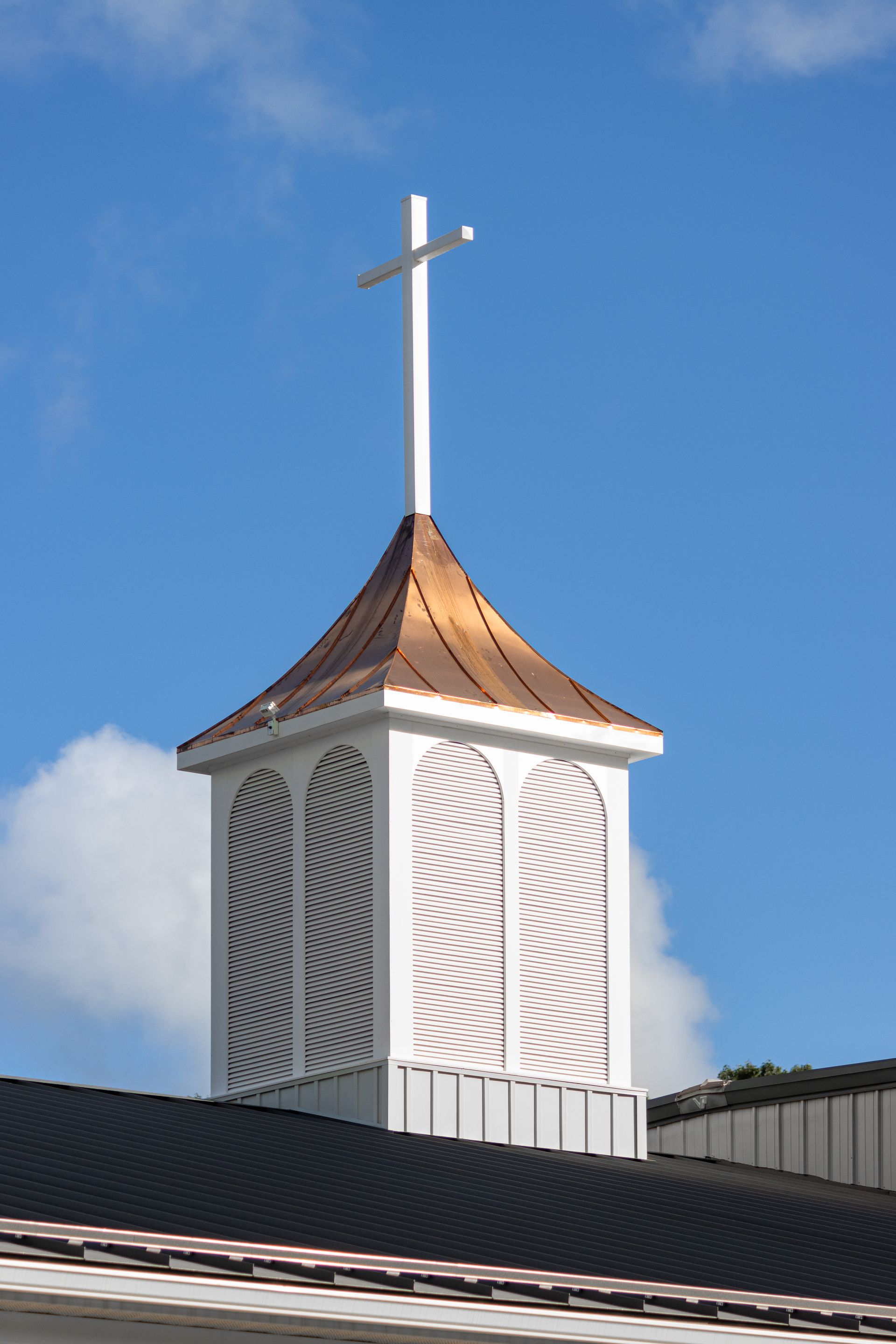 White church steeple with copper roof and cross, against a blue sky.