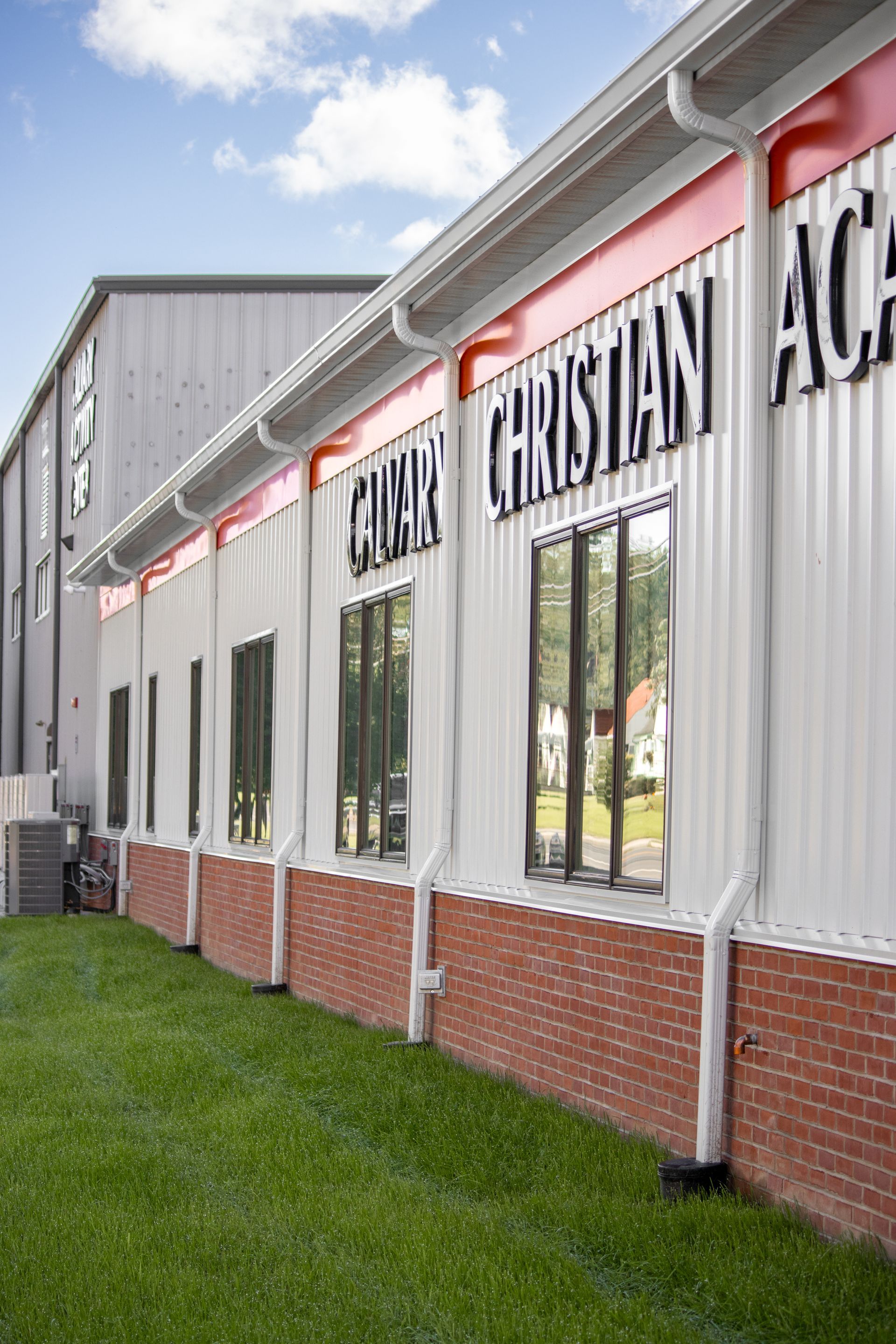 Exterior of Conway Christian Academy; white corrugated metal walls with red trim, brick base, and grass.