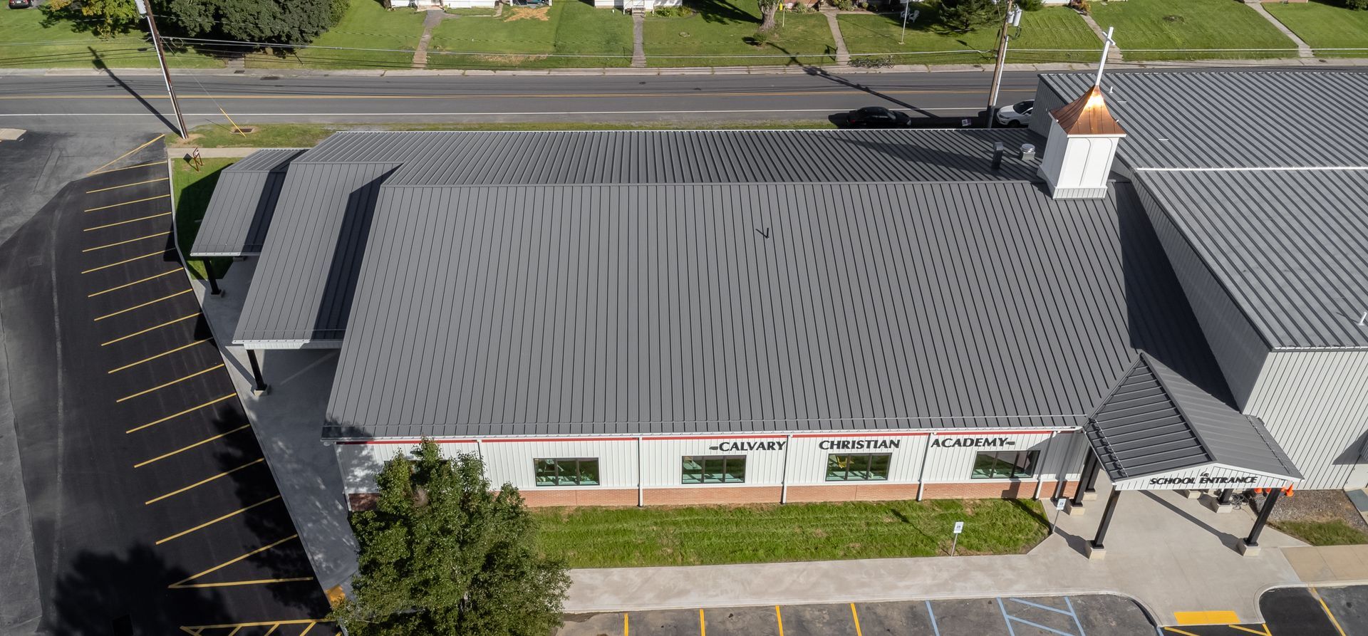 Aerial view of a building with a patterned gray roof and small white steeple.