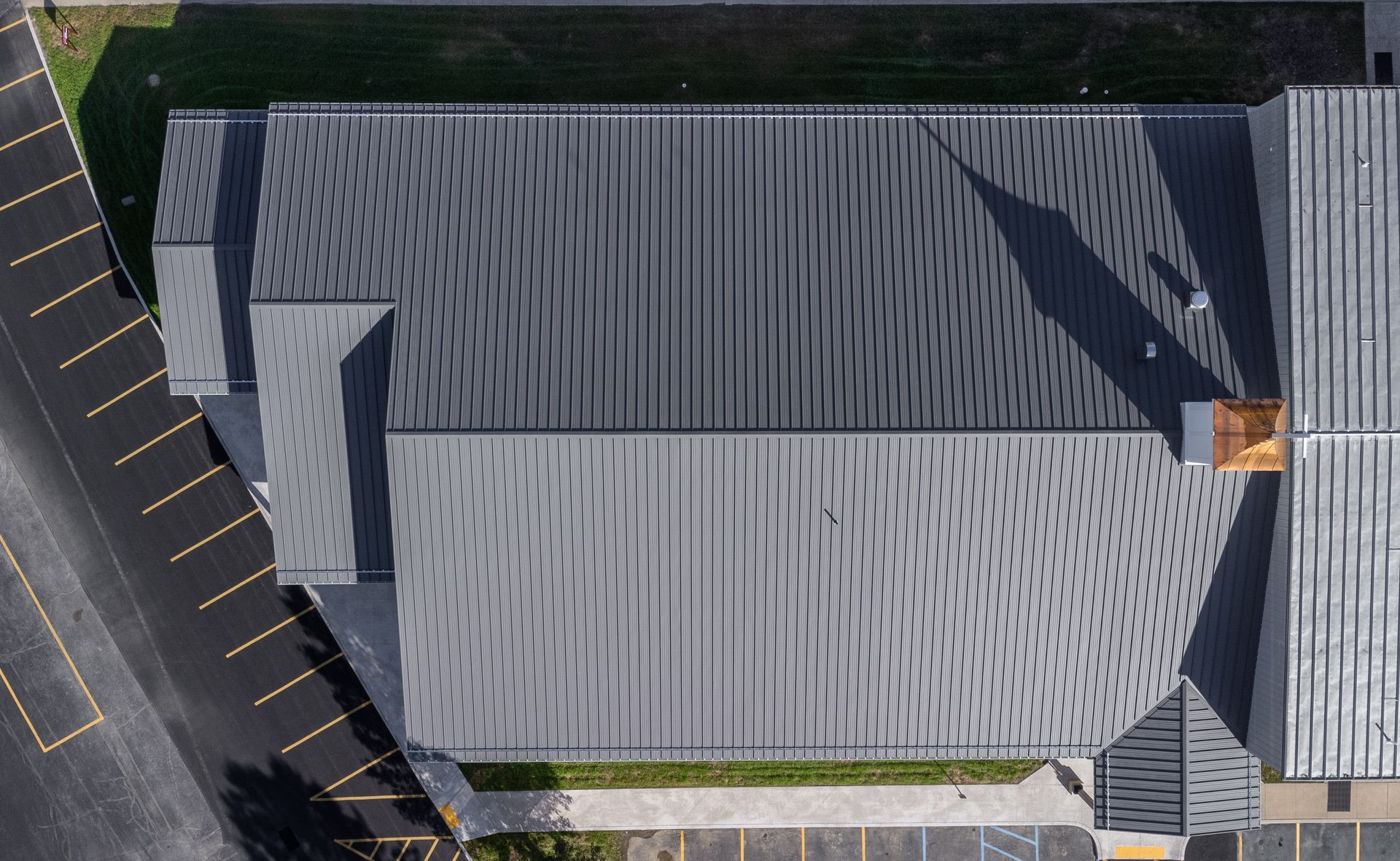 Overhead view of a gray building with patterned roof, adjacent to a parking lot and road.
