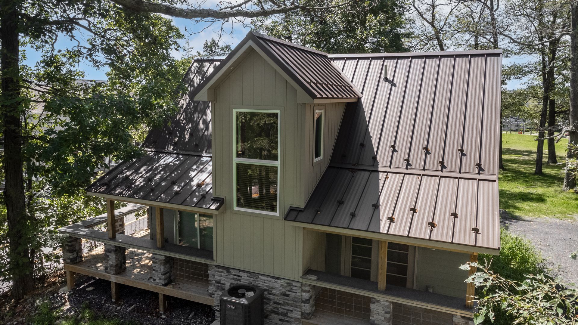 Two-story house with a metal roof and green siding. It has a stone base and a large window.
