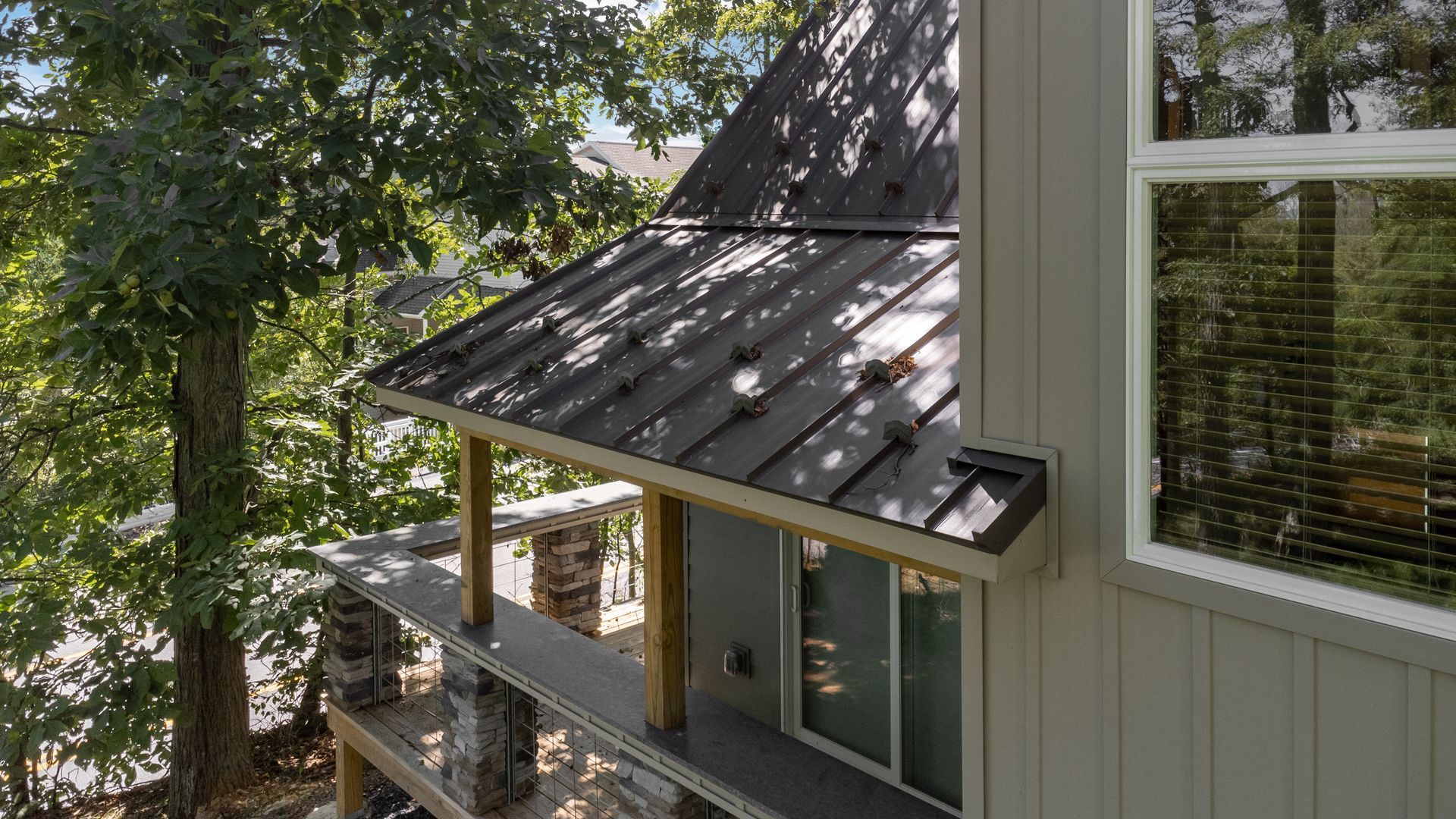 A house with a metal roof, porch, and large window, surrounded by trees.