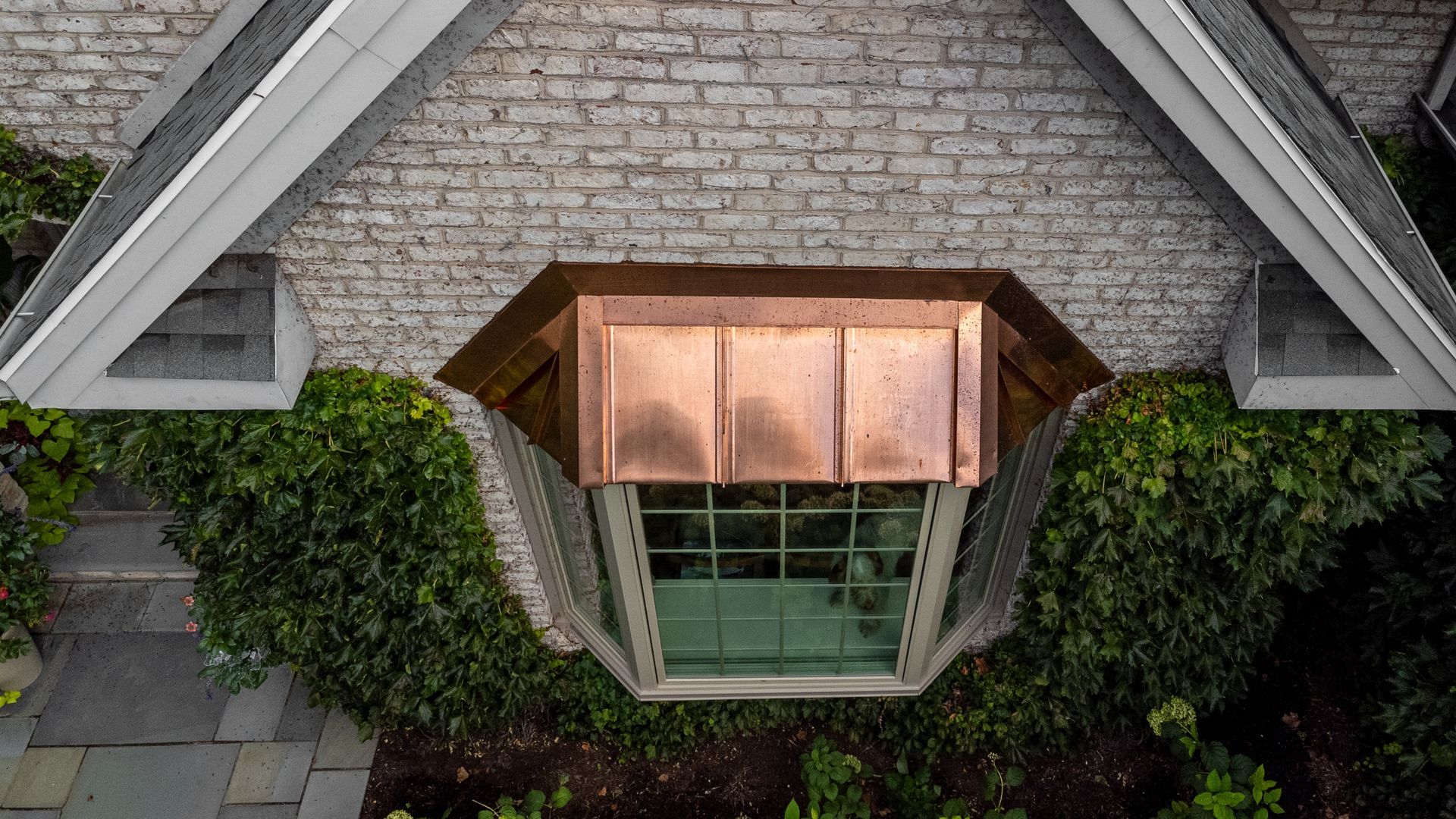 Overhead view of a copper-roofed window framed by ivy on a brick building.