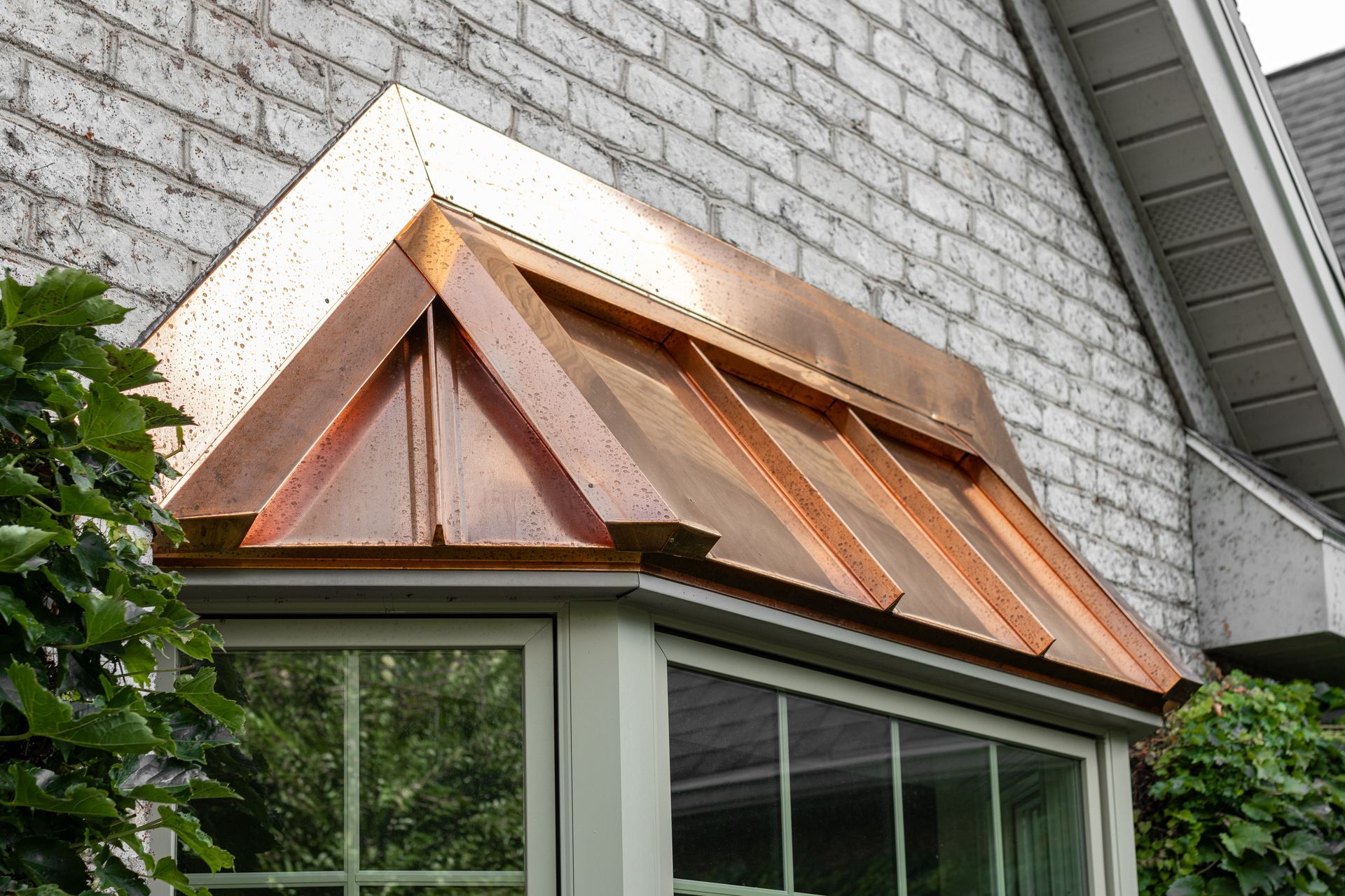Copper-roofed bay window on a brick-sided house.