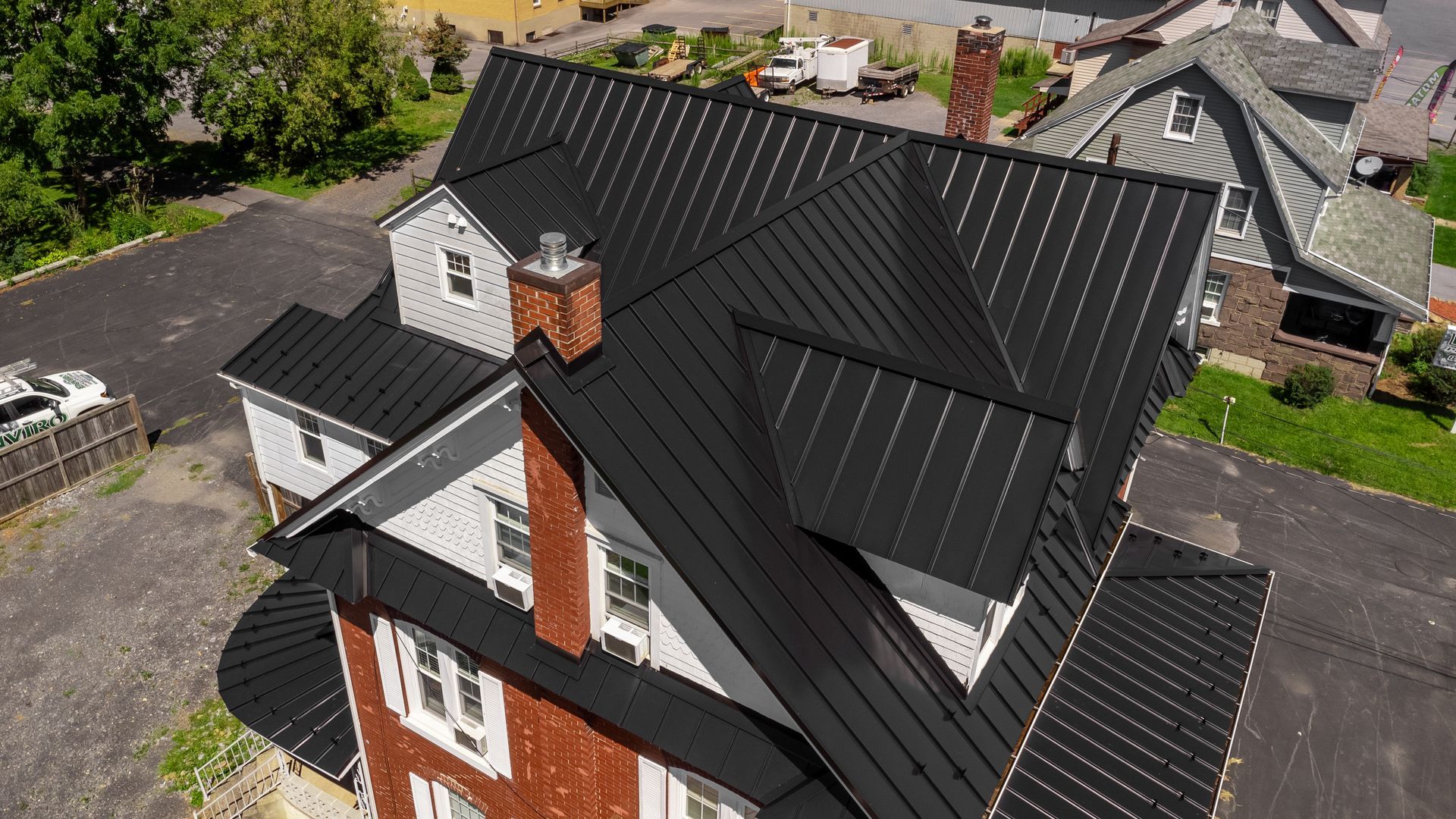 Black metal roof on a two-story house with a brick chimney and white siding.