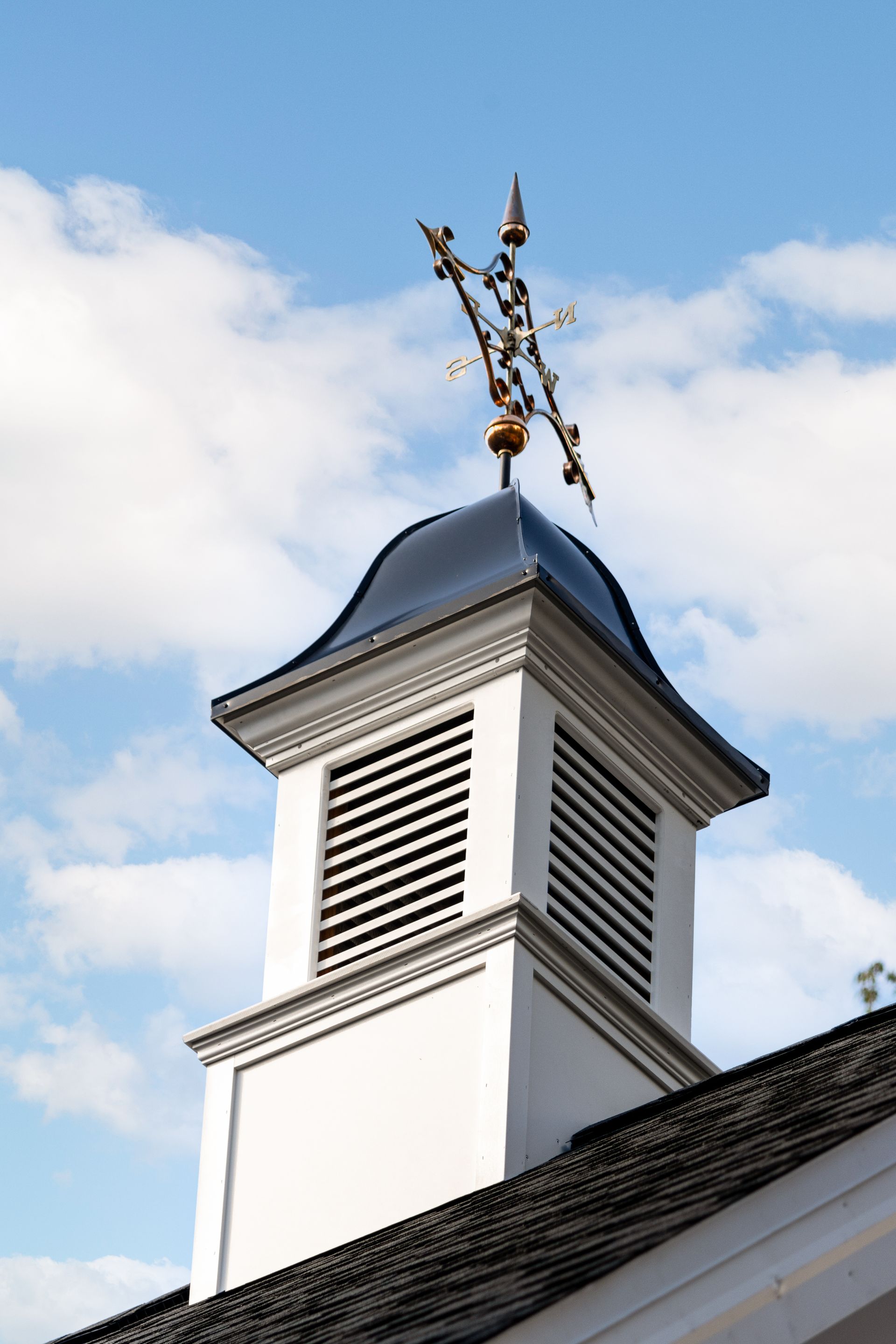 White cupola with dark roof, gold weather vane, blue sky and clouds.