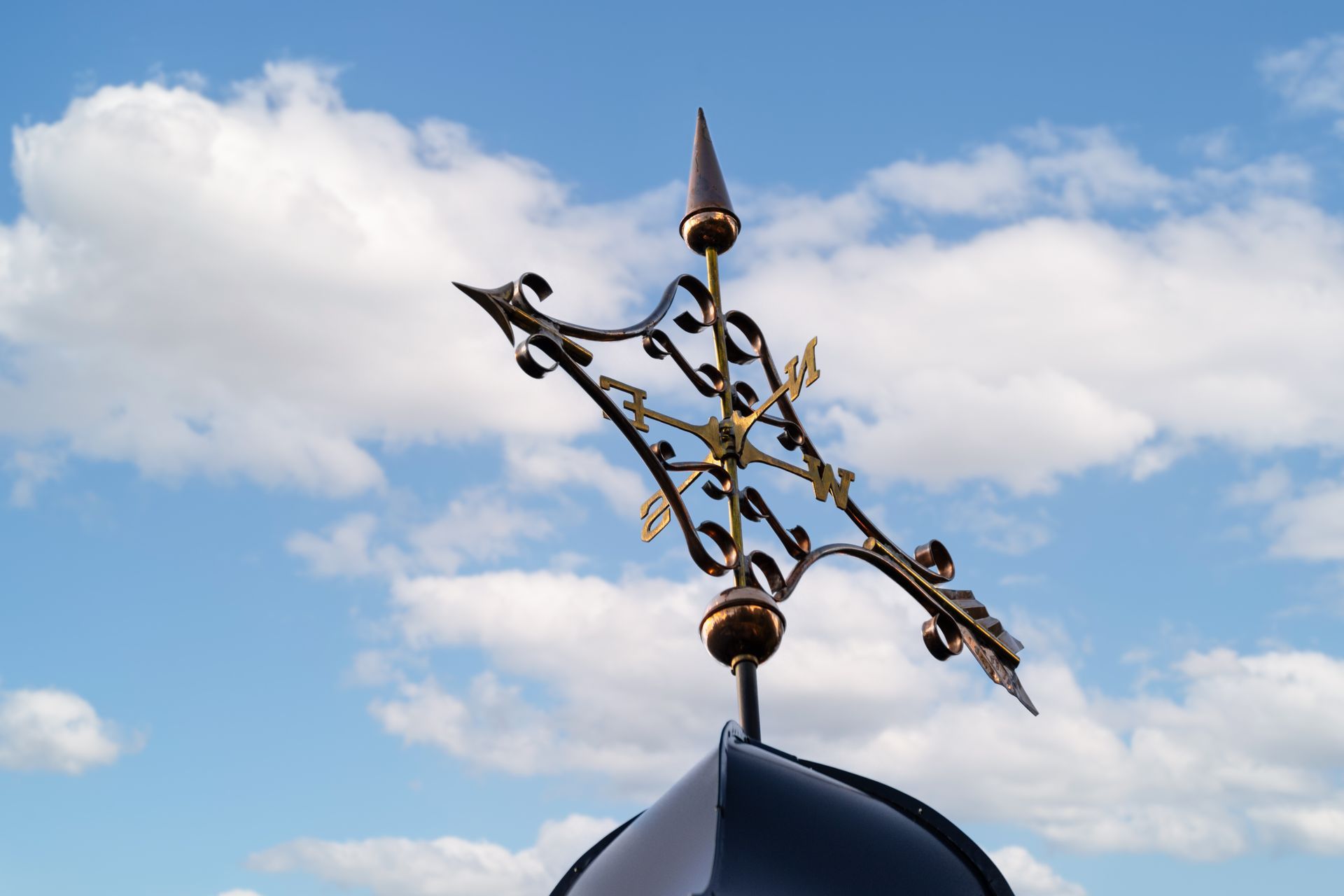 Ornate weather vane against a cloudy blue sky.