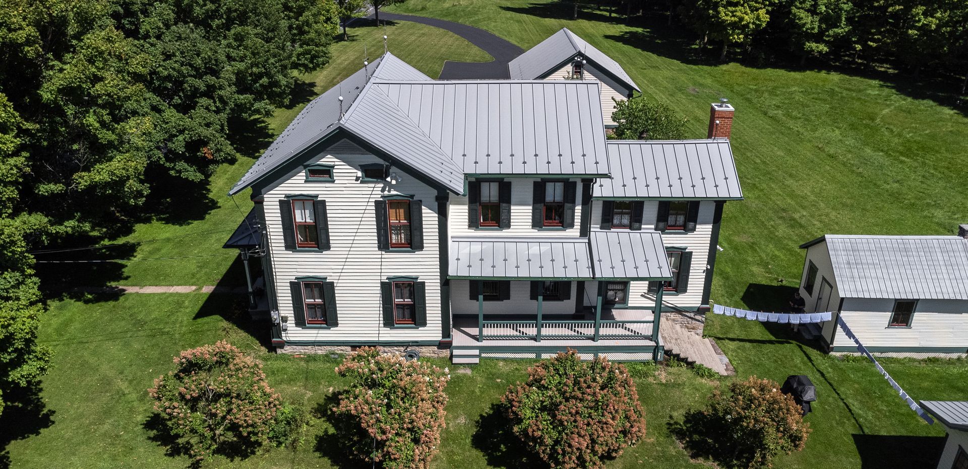 Aerial view of a white farmhouse with a metal roof on a grassy hill.