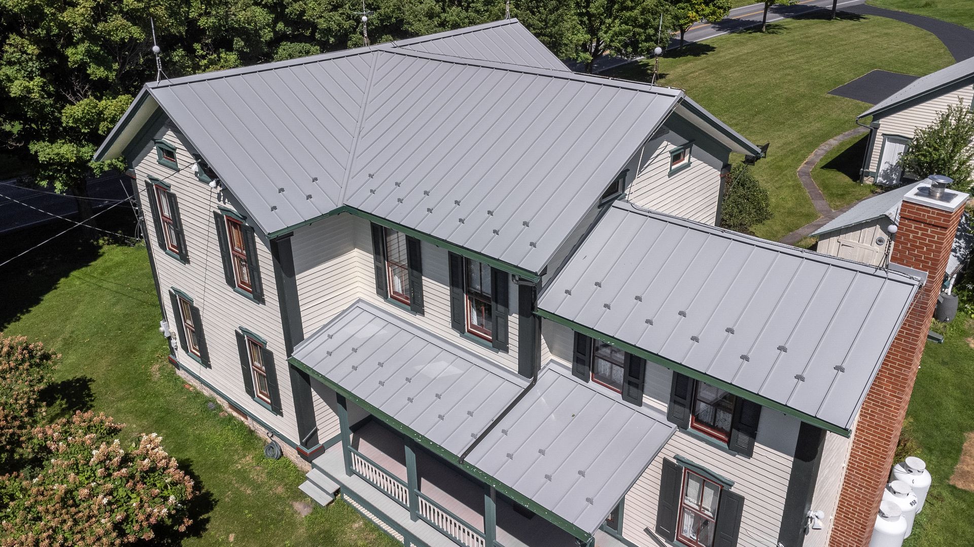 Aerial view of a two-story house with a gray metal roof, cream siding, and green trim.
