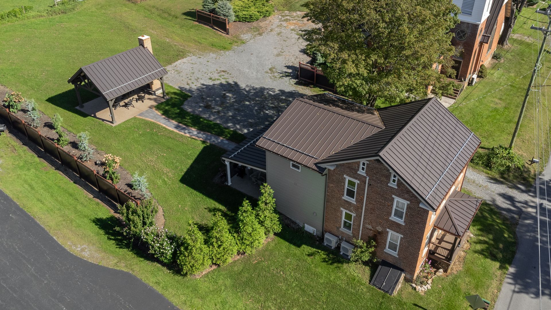 Aerial view of a house with a brown metal roof and a small adjacent structure; surrounded by green grass.