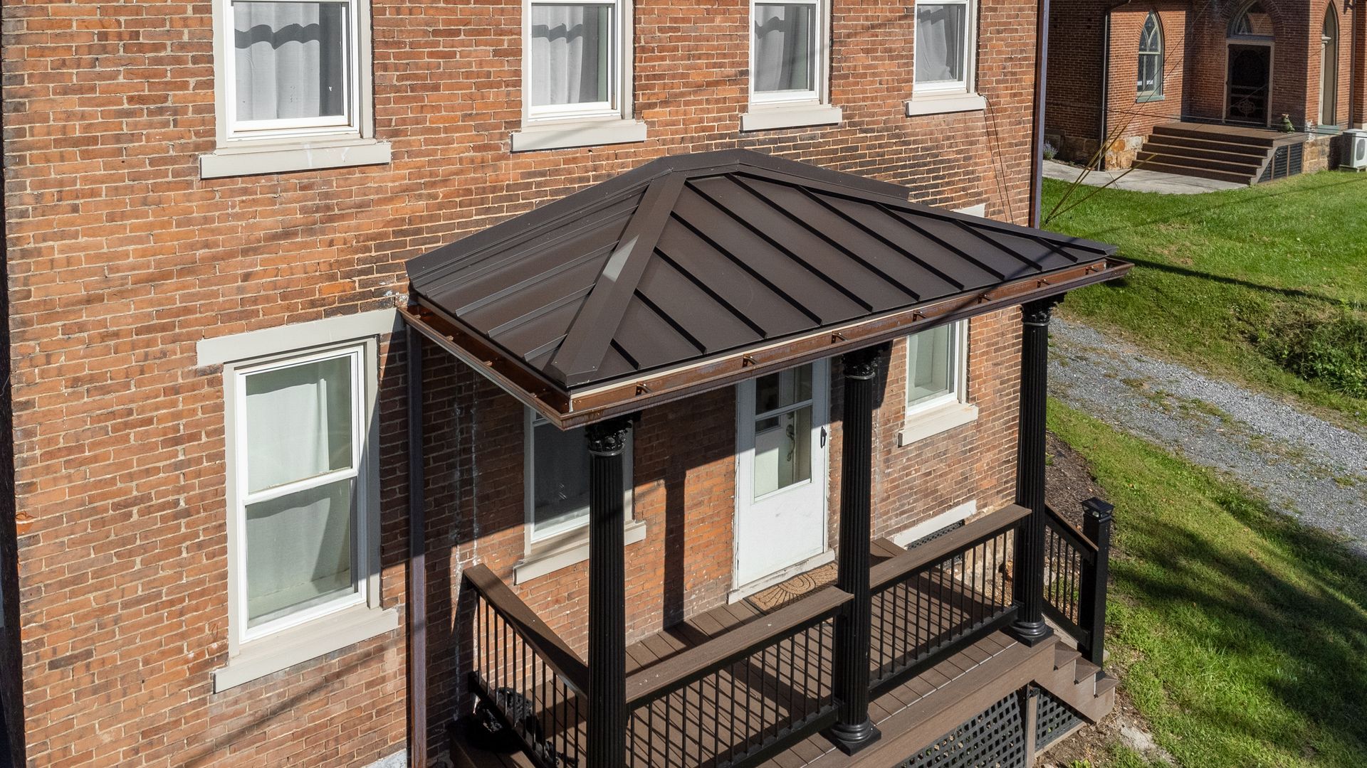 Brick building with a black metal roof porch supported by columns and a railing.