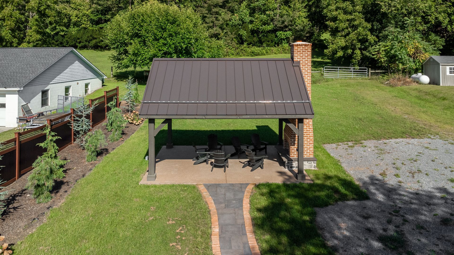 Brown shelter with metal roof, brick chimney, picnic tables, on a grassy lawn.