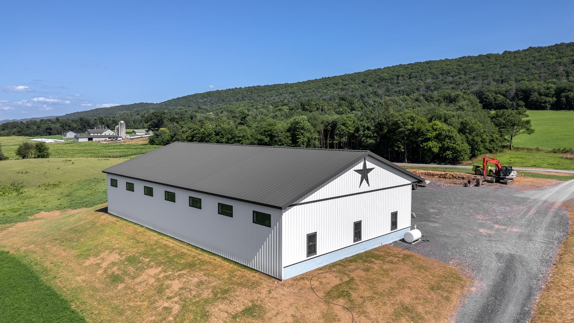 White barn with black trim and a star, in a rural setting with hills and blue sky.