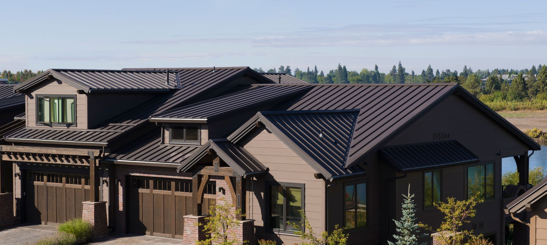 Modern house with dark gray metal roof and brick exterior in a sunny rural setting