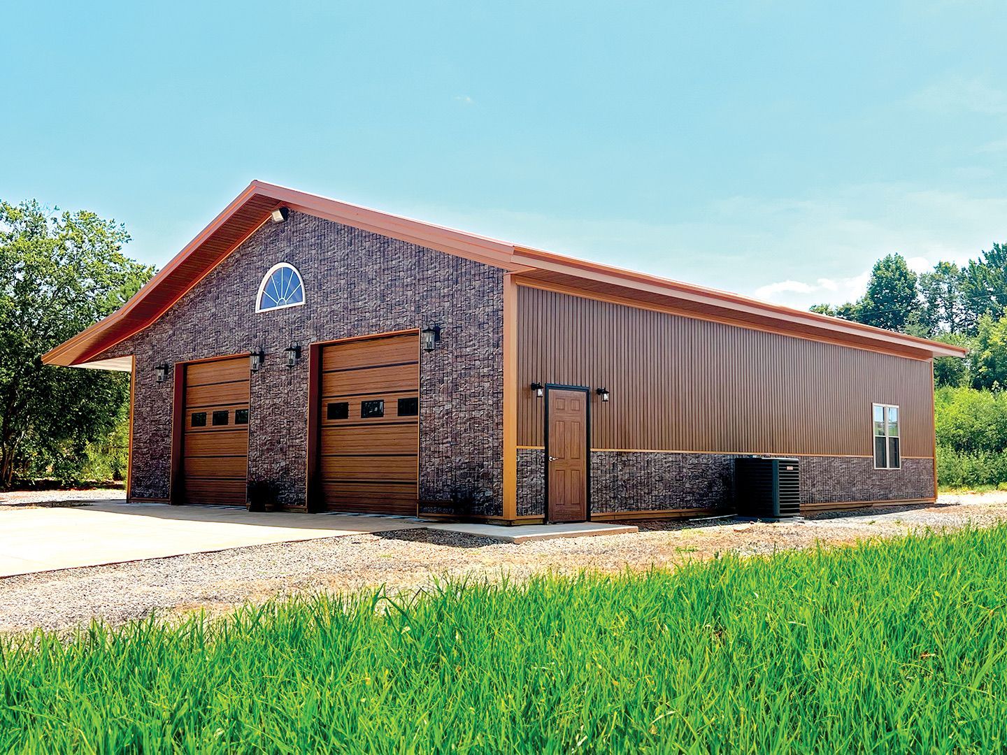 Tan and brown metal garage with two bays and a gravel driveway.