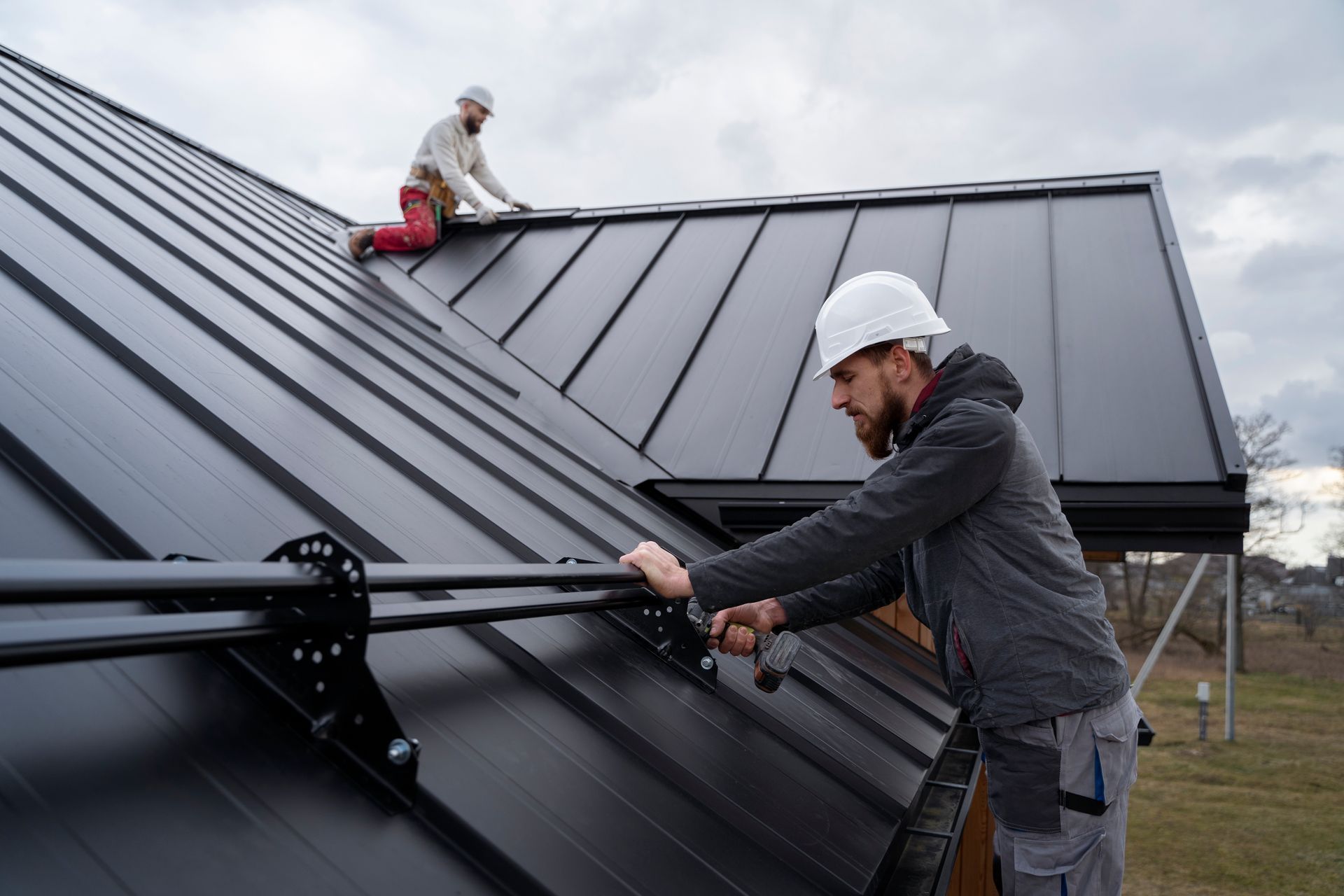 Workers installing a black metal roof on a building, one kneeling on the roof in Central PA