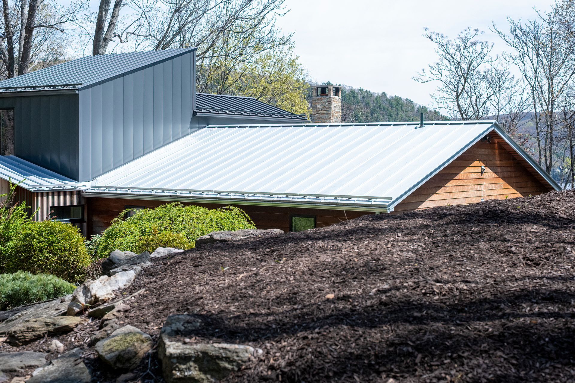 Modern house in Central PA with white metal roof beside large dark mulch mound and spring trees