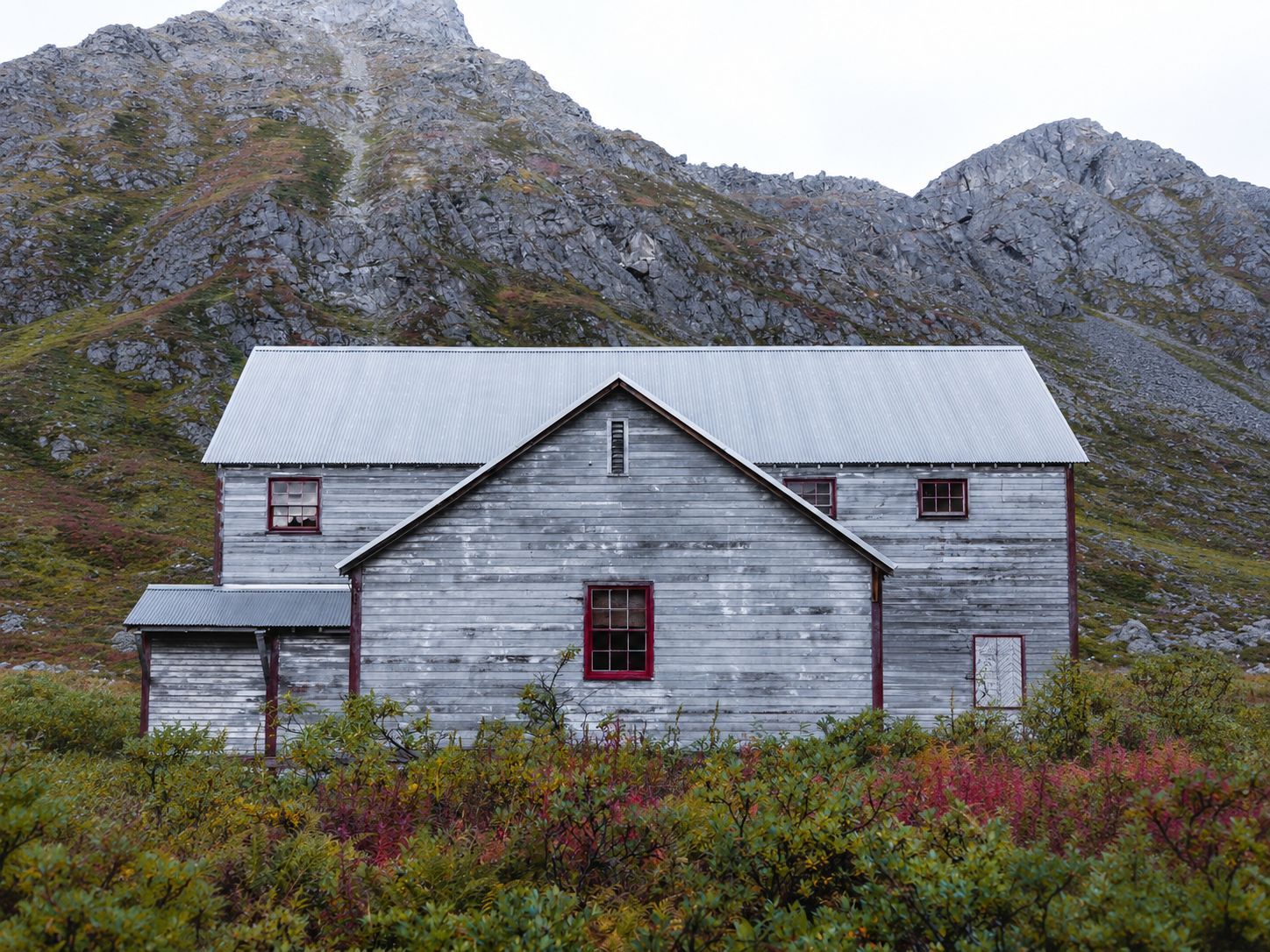 Weathered gray house with red windows in a rugged Central PA mountain landscape under an overcast sk