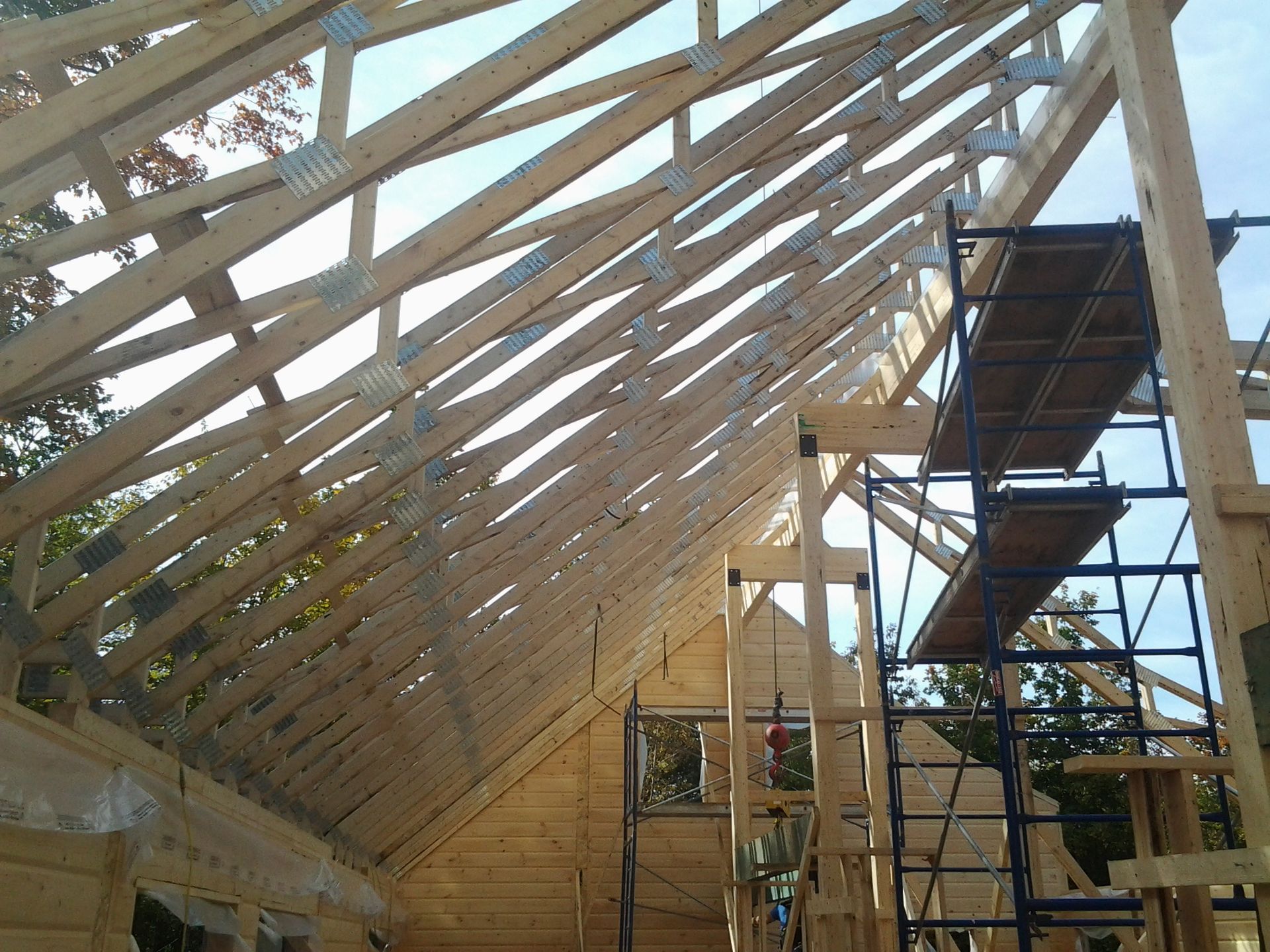 Charpente de toit en bois avec échafaudages dans une cabane en rondins en construction, lumière vive du soleil.