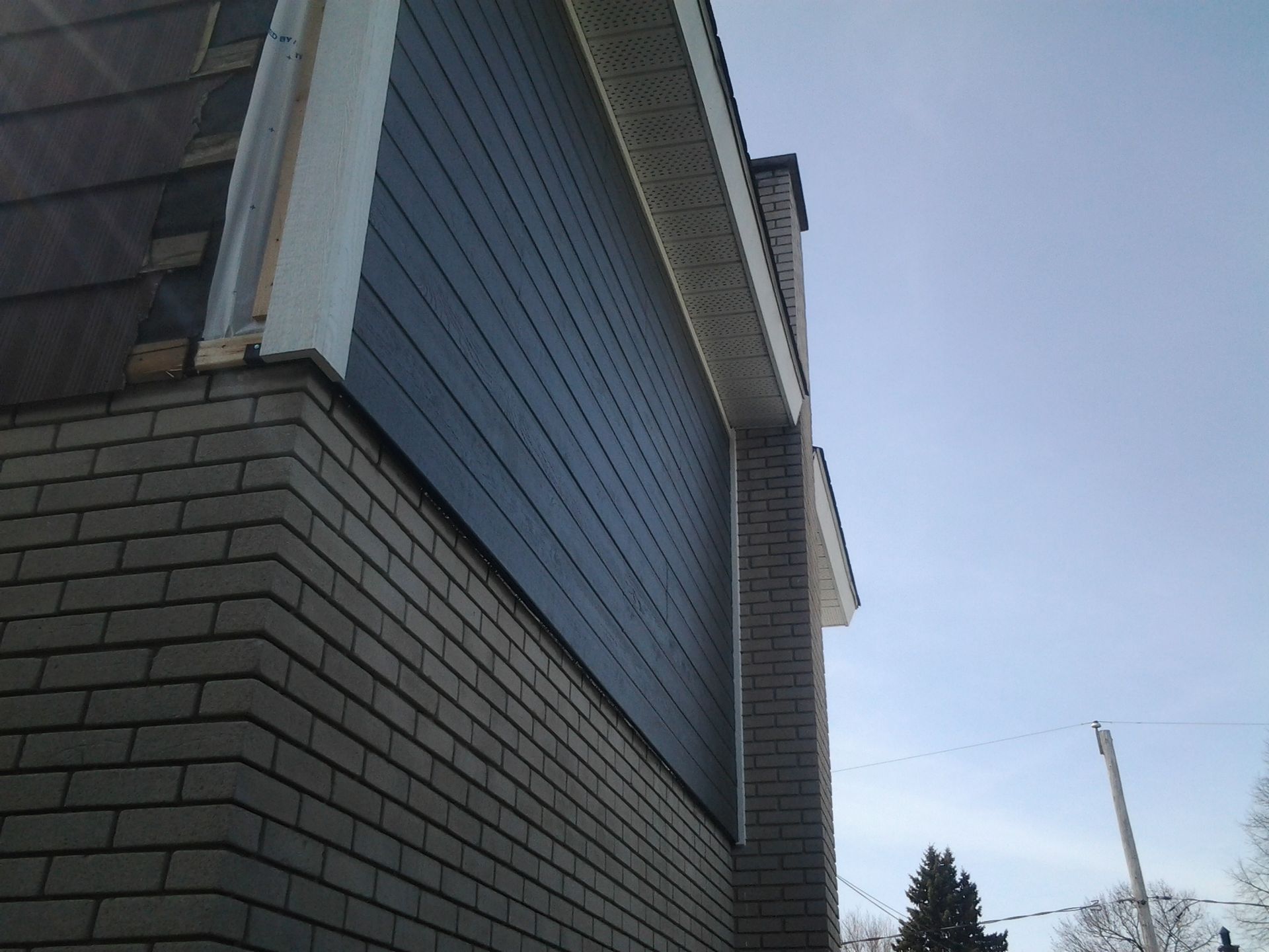 Extérieur d'une maison en briques et bardage bleu, avec une cheminée et un ciel dégagé.