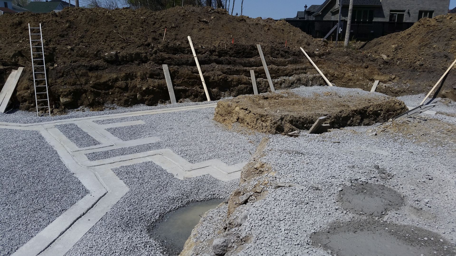 Chantier de construction avec gravier, coffrages en béton et tas de terre ; ensoleillé à l'extérieur.