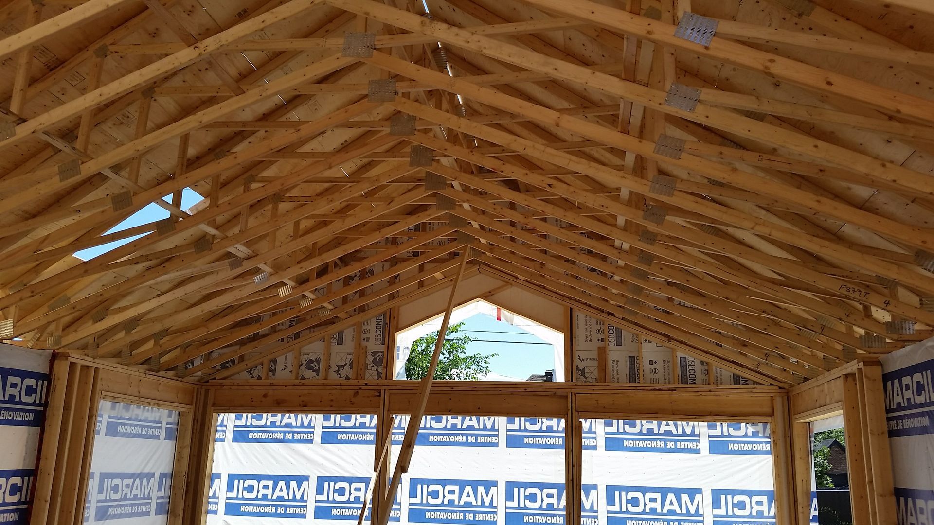 Charpente en bois soutenant l'intérieur d'une maison en construction ; une fenêtre se trouve au centre.