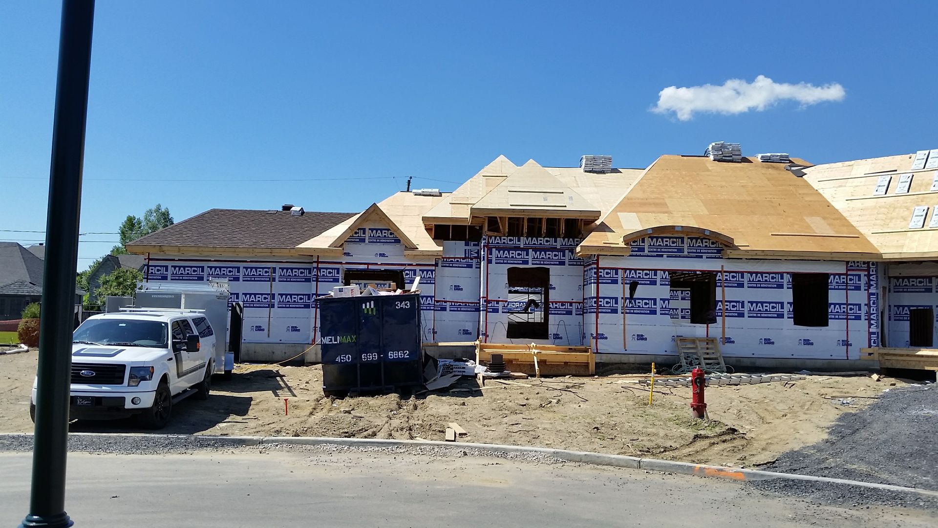 Construction d'une maison à ossature apparente et bâche bleue. Camion blanc et benne à ordures devant.