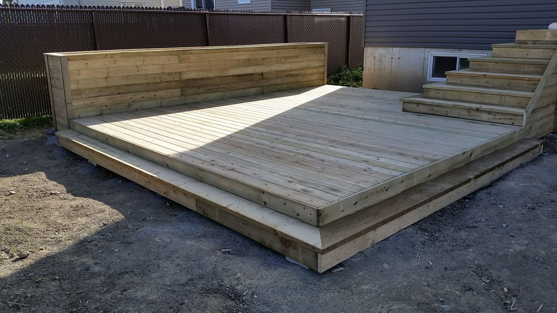 Terrasse en bois avec marches et muret, à l'extérieur sur gravier.