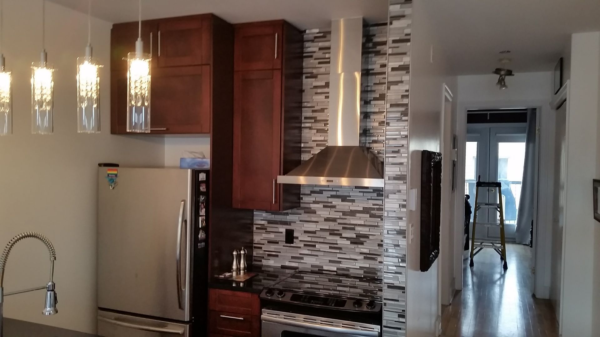Petite cuisine avec appareils électroménagers en acier inoxydable, armoires en bois foncé et crédence en carrelage décoratif.