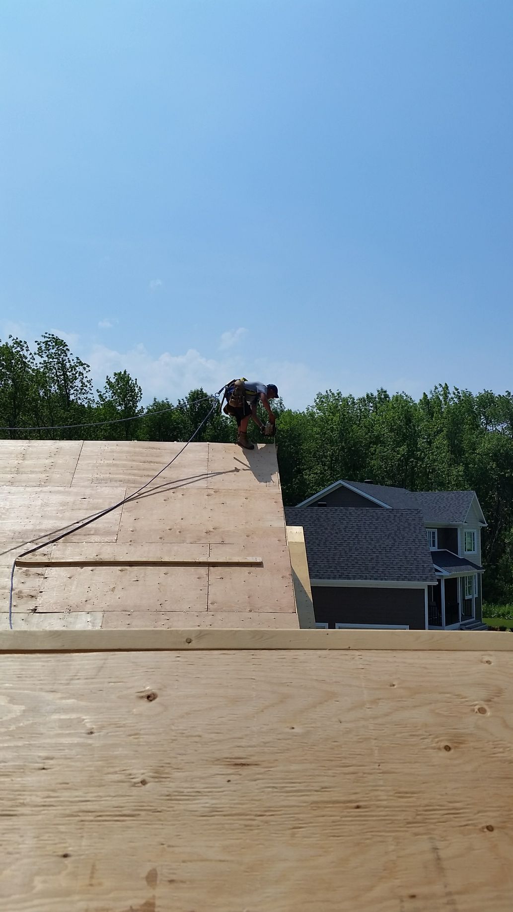 Personne travaillant sur un toit. Journée ensoleillée, arbres, maison en arrière-plan.