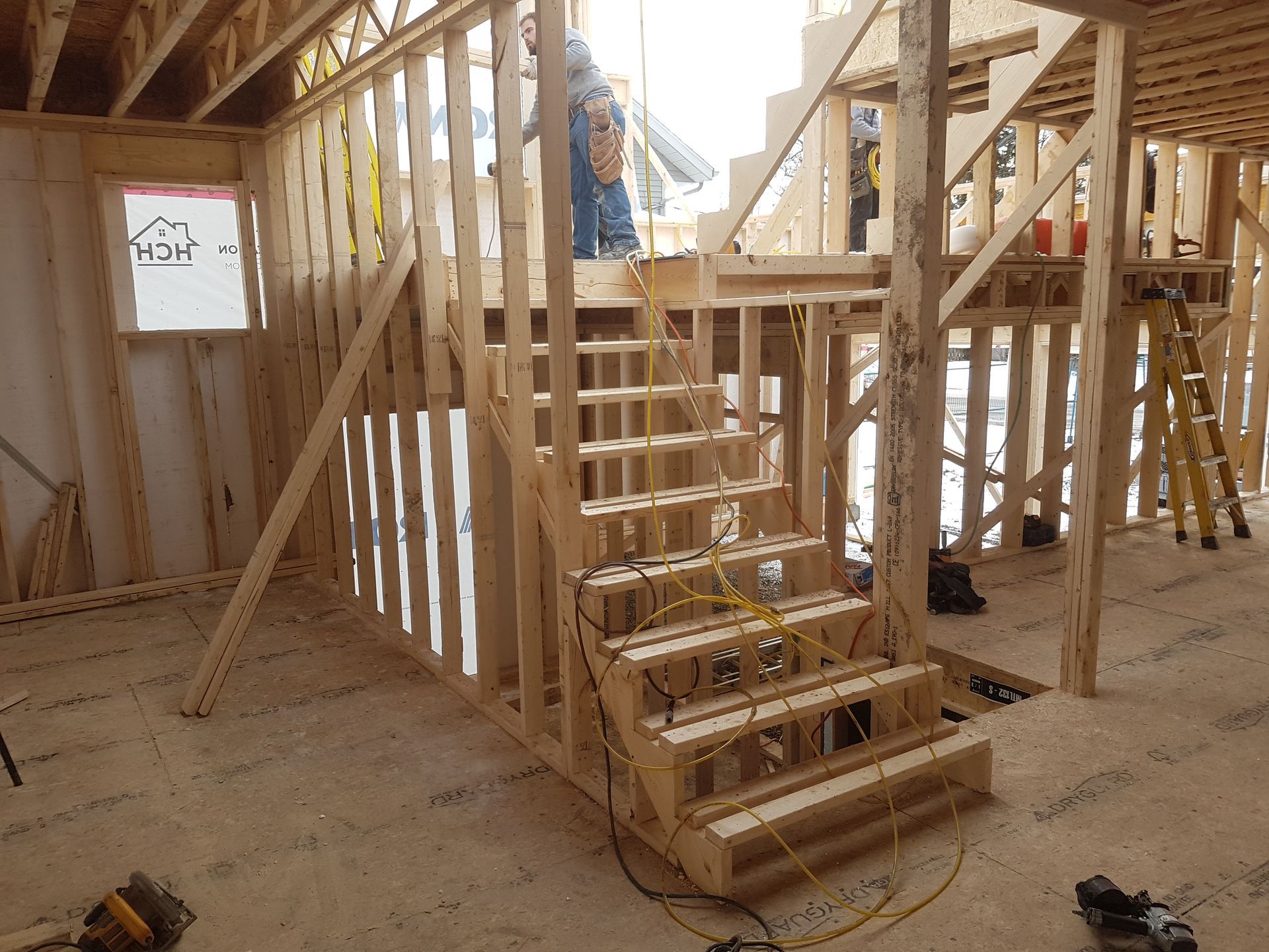 Escalier à ossature bois en construction à l'intérieur d'un bâtiment, avec une personne debout sur le palier supérieur.