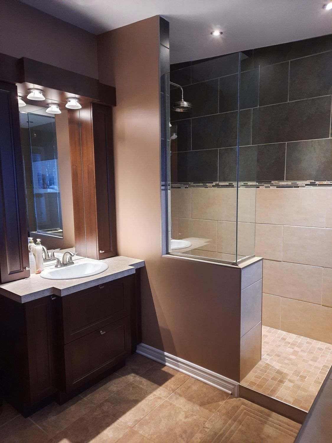 Salle de bains avec meuble-lavabo en bois foncé, douche en verre et murs marron.