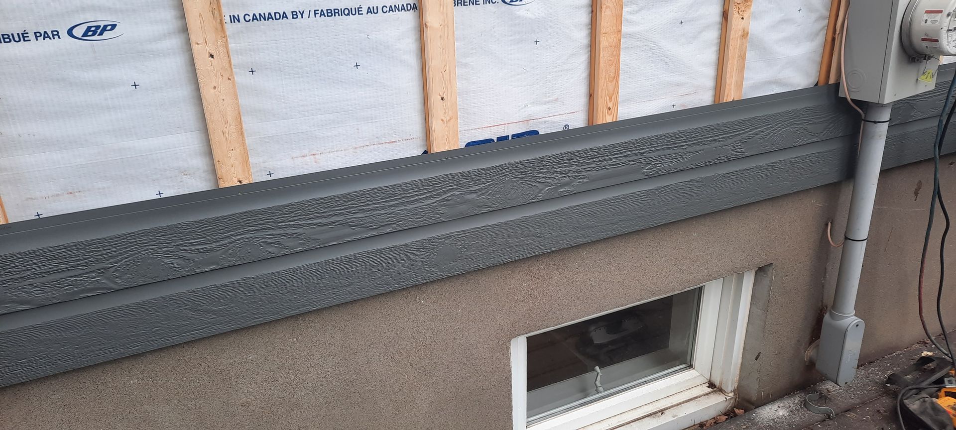 Extérieur d'un bâtiment en construction, montrant la charpente, le bardage et les conduits électriques.