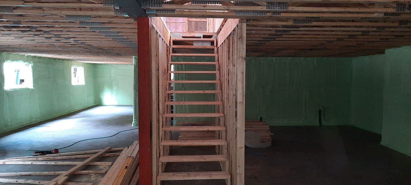 Escalier en bois dans un sous-sol non aménagé, bordé de murs verts et de poutres apparentes au plafond.