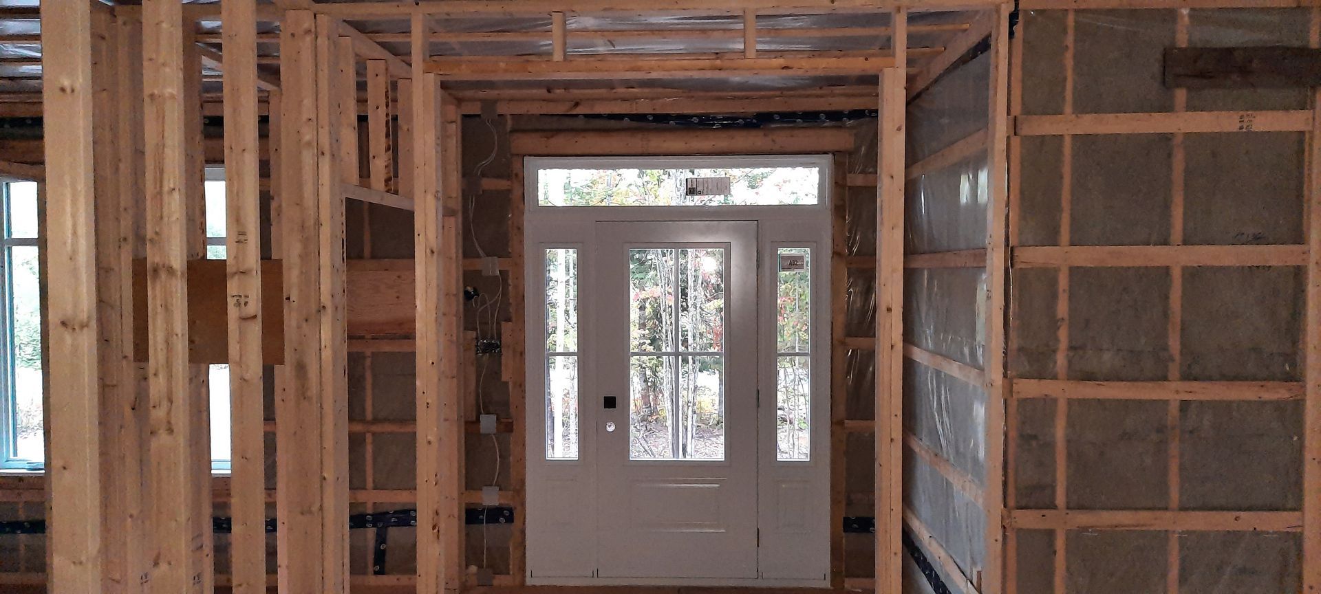 Intérieur d'une maison en construction. Une ossature en bois entoure une porte d'entrée blanche. L'isolation est visible.