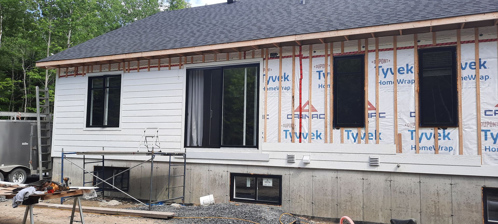 Une maison en construction. Murs extérieurs avec fenêtres recouverts de film Tyvek noir et charpente apparente.