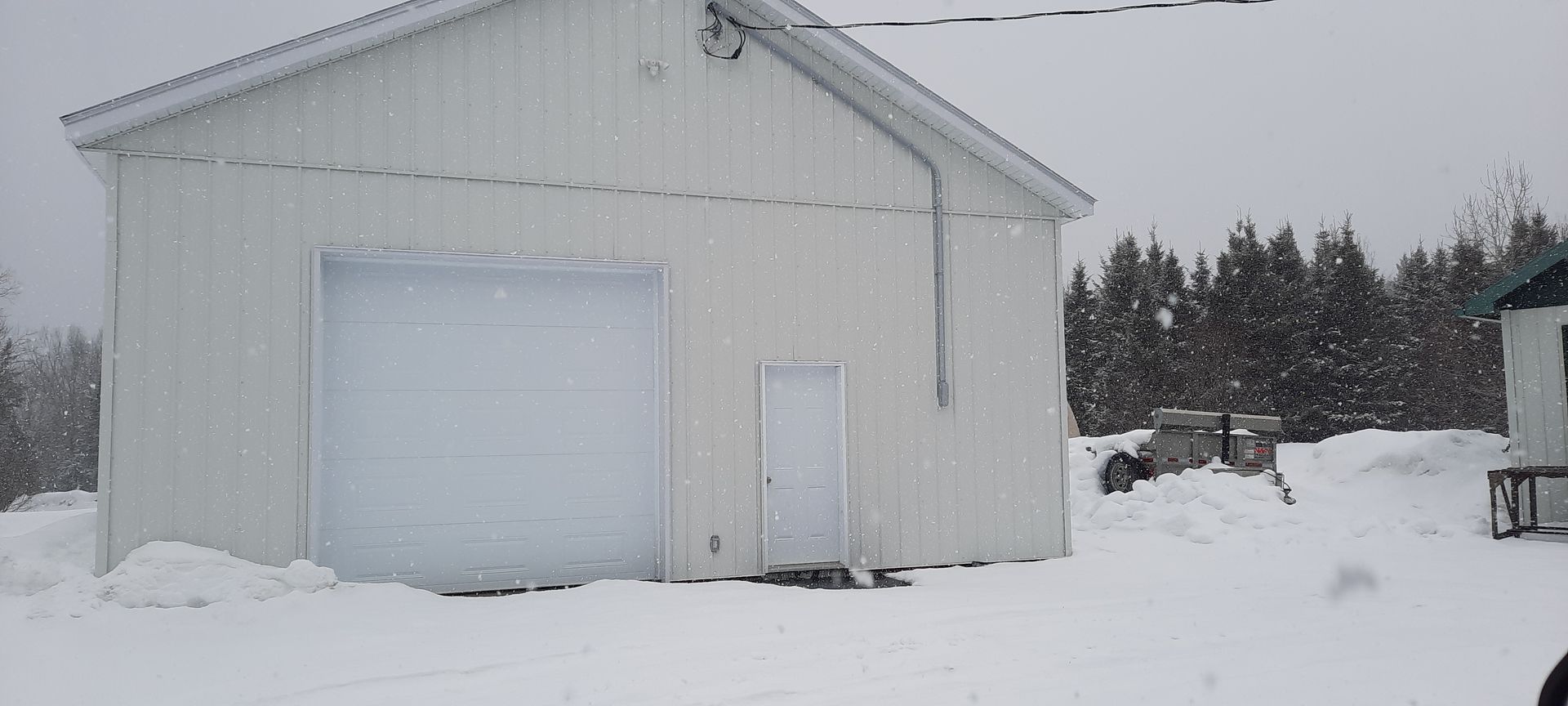 Scène enneigée avec un bâtiment blanc, une porte de garage et une petite porte. La neige recouvre le sol.