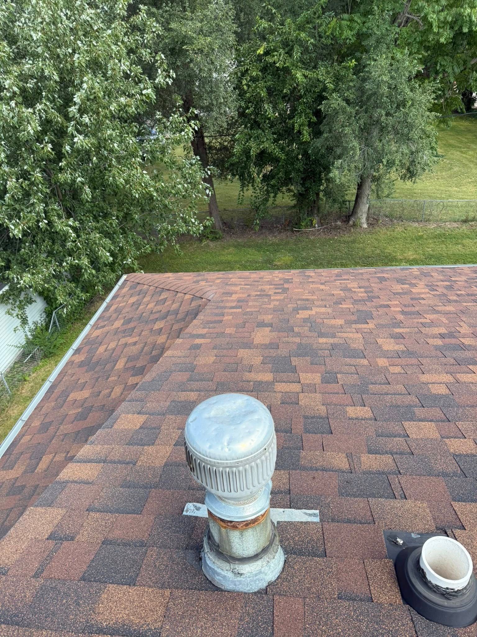 A view from above showing a brown shingled roof with a metal ventilation cap and a small, circular pipe opening.