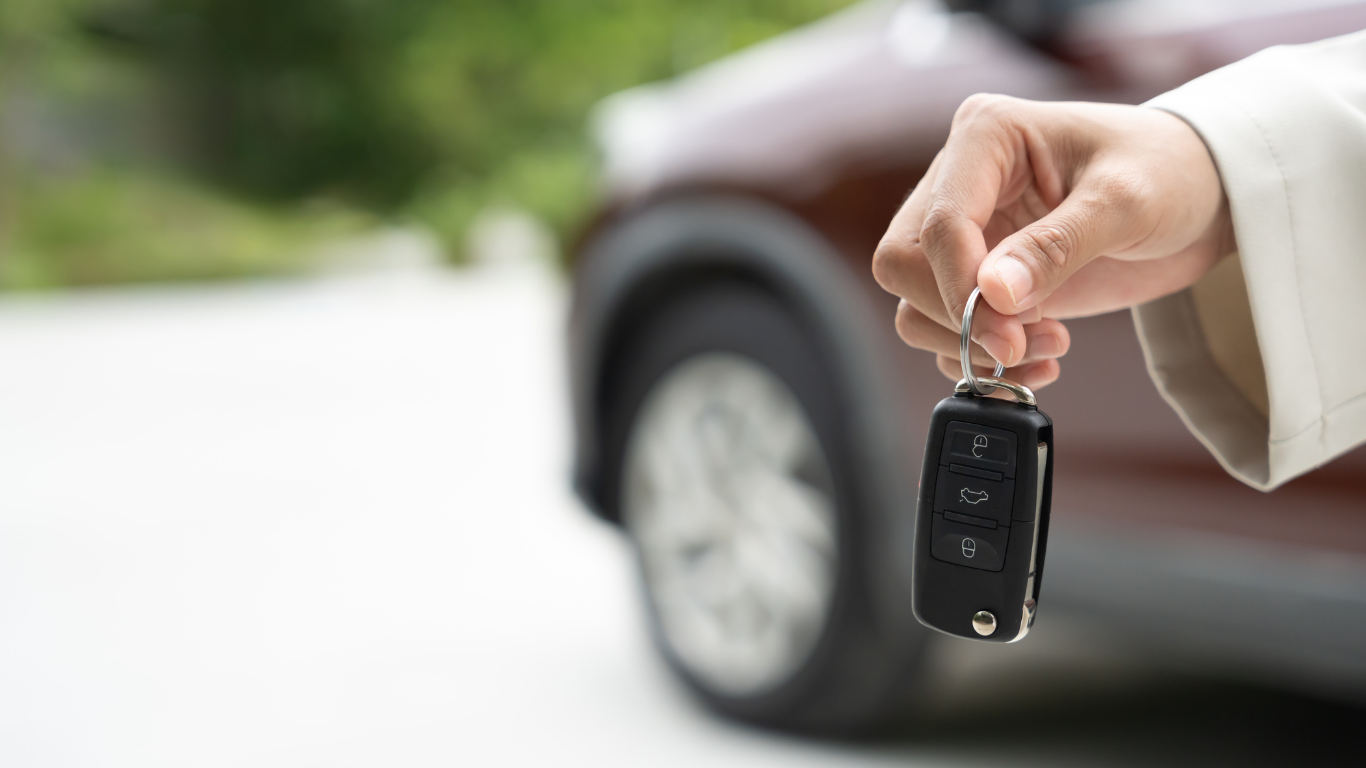 Hand holding car keys with a brown car in the background.