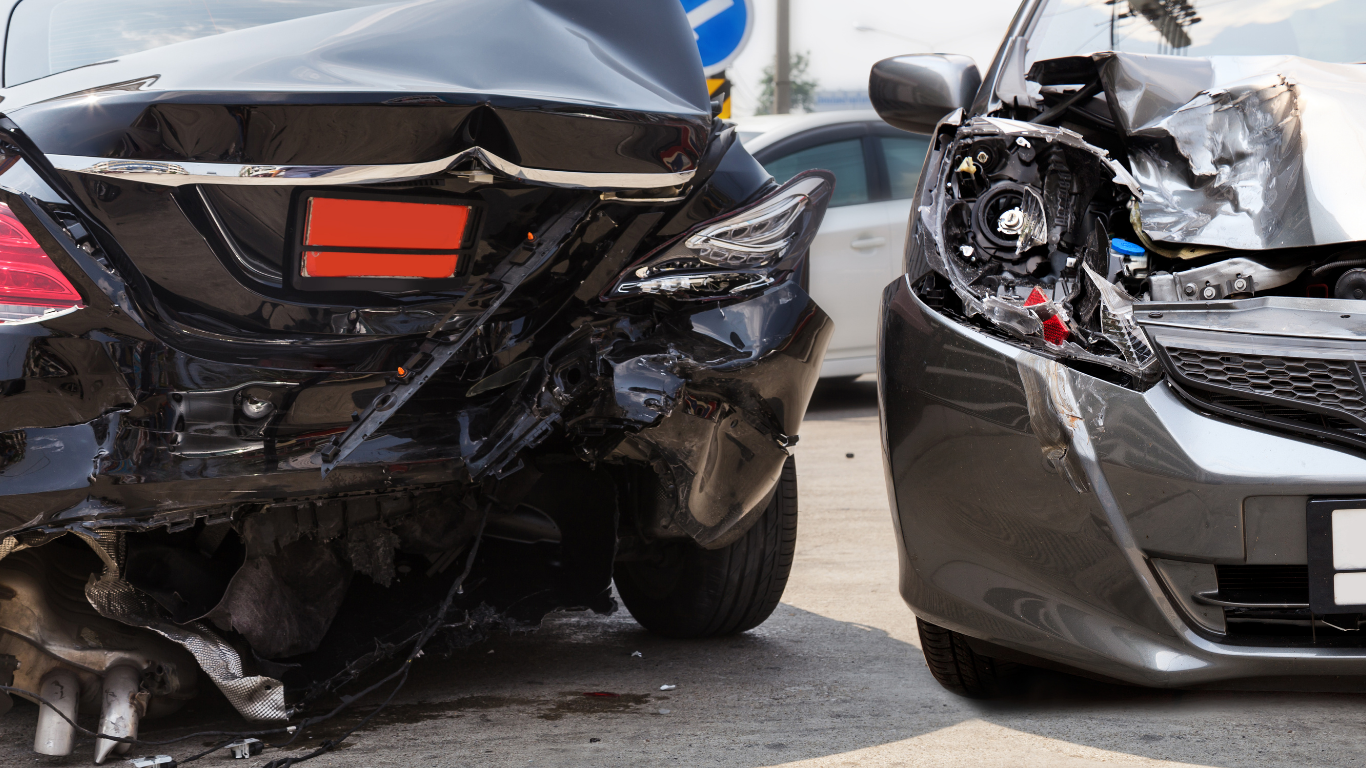 Two cars severely damaged in a collision; black car rear-ended, grey car front end crushed.