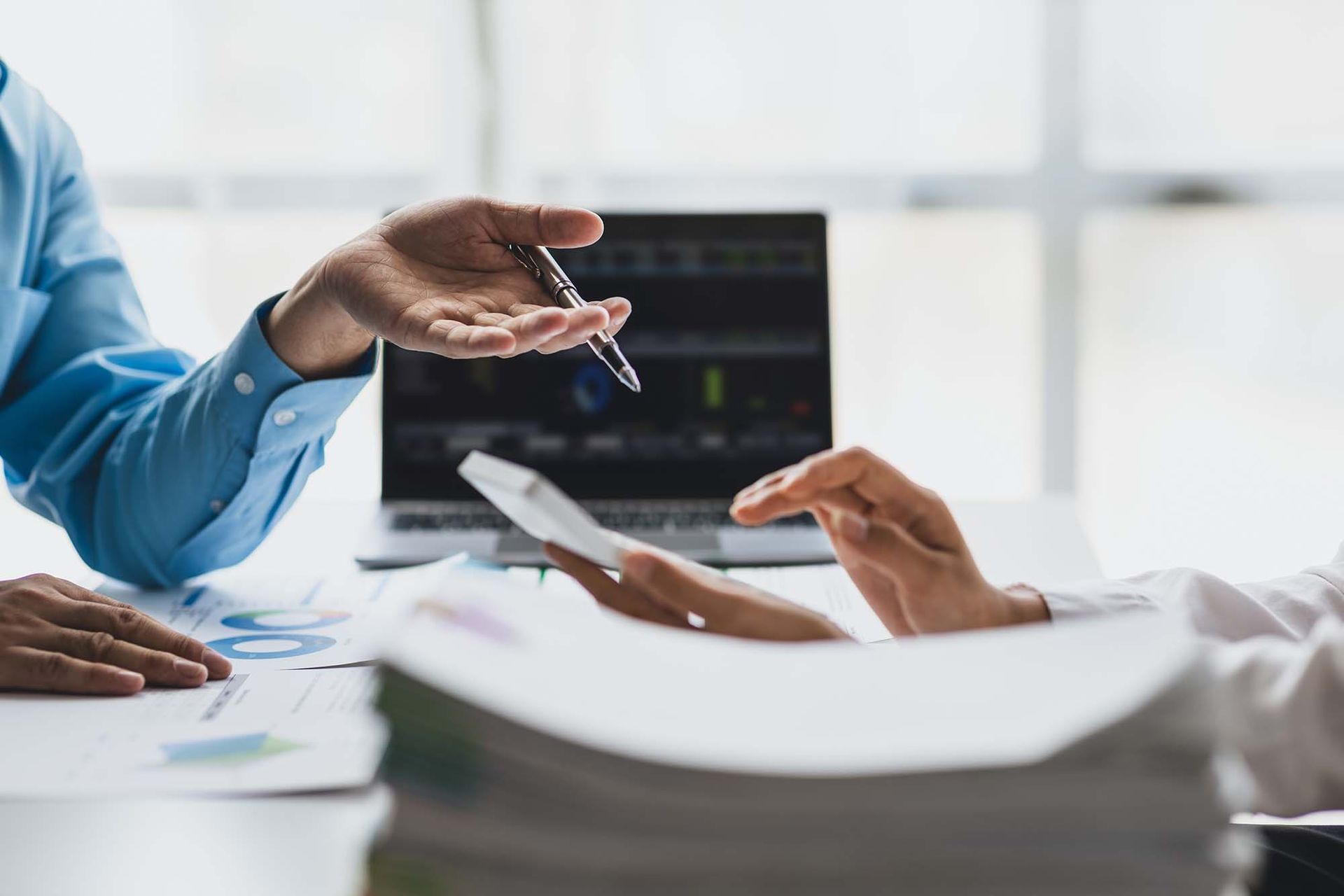 Hands exchanging a document across a desk in a bright office meeting