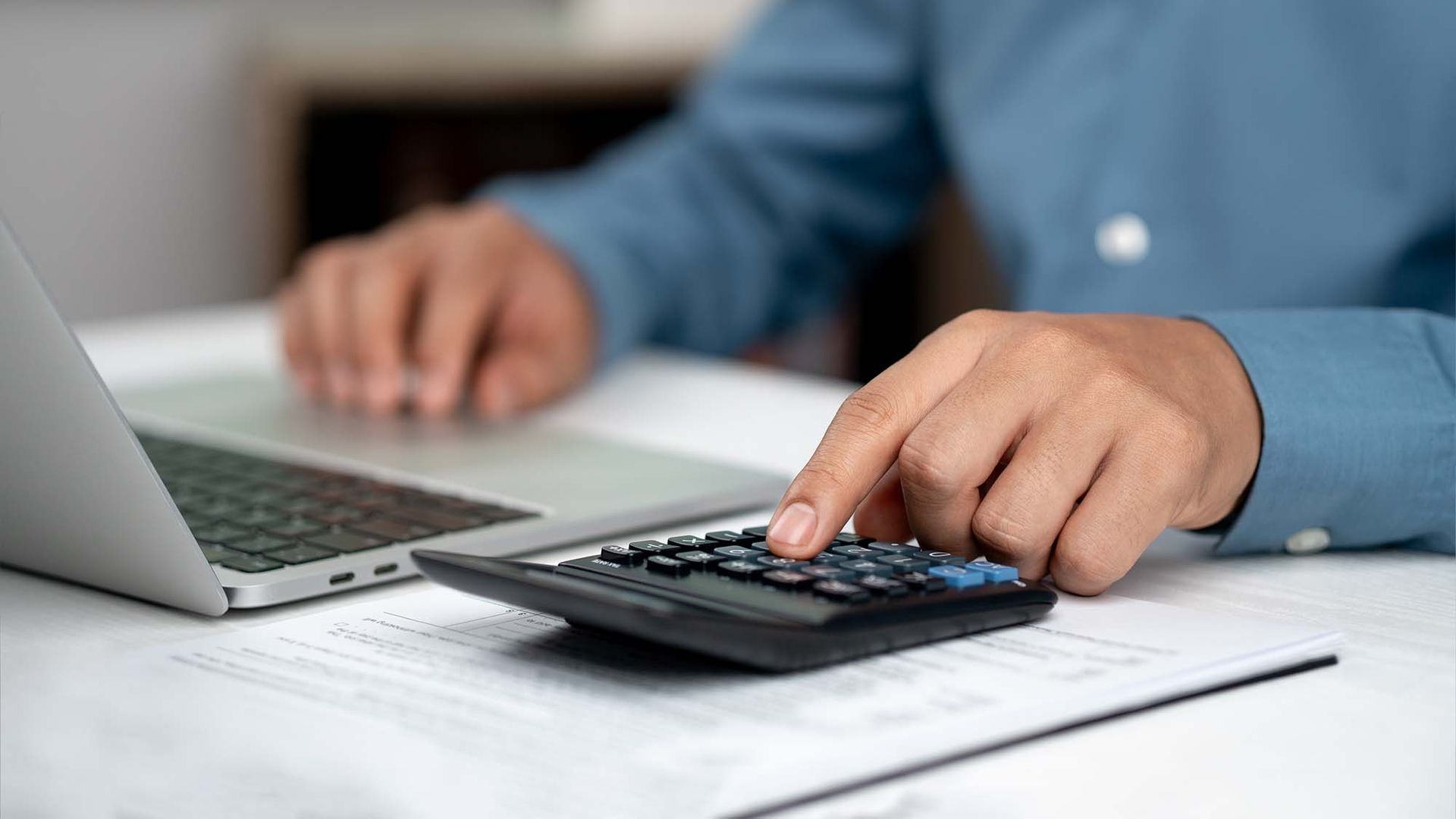Person using a calculator beside a laptop at a desk