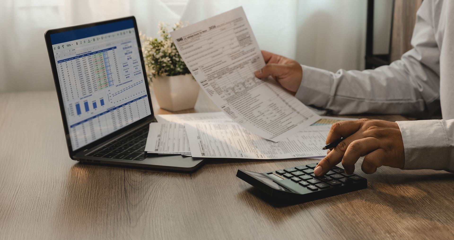Two people review papers beside a laptop showing charts, with a calculator on the desk.